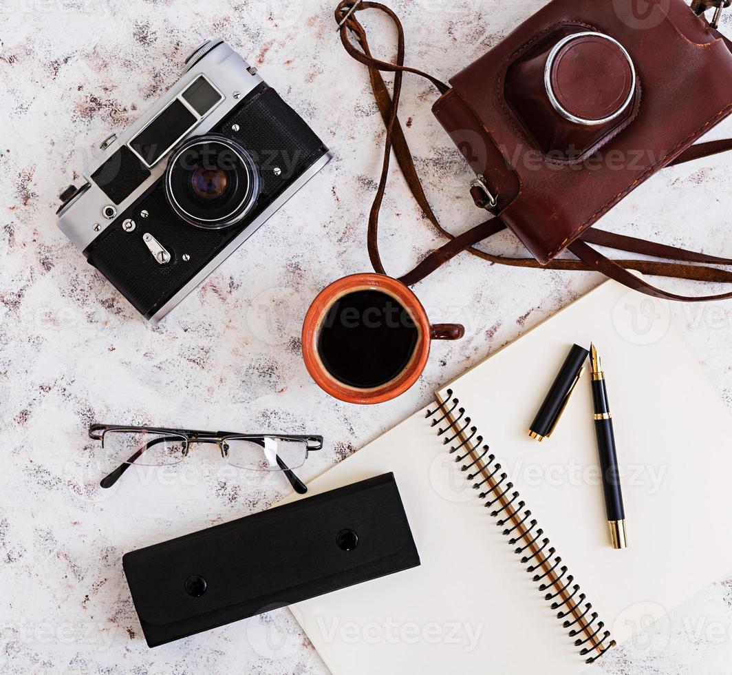 Flat lay, top view office table desk. Desk workspace with retro camera, diary, pen, glasses, case, cup of coffee on white background. photo