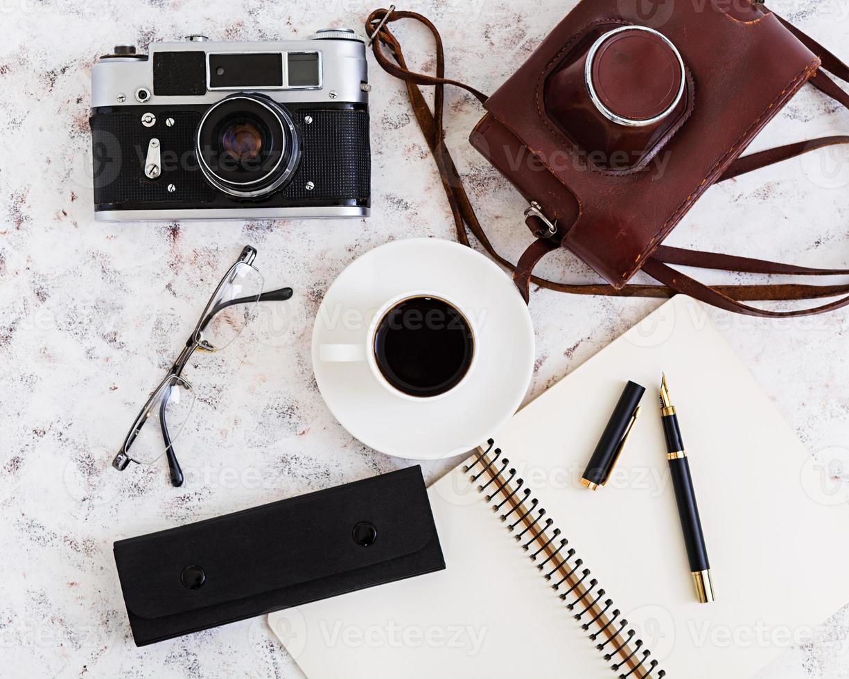 Flat lay, top view office table desk. Desk workspace with retro camera, diary, pen, glasses, case, cup of coffee on white background. photo