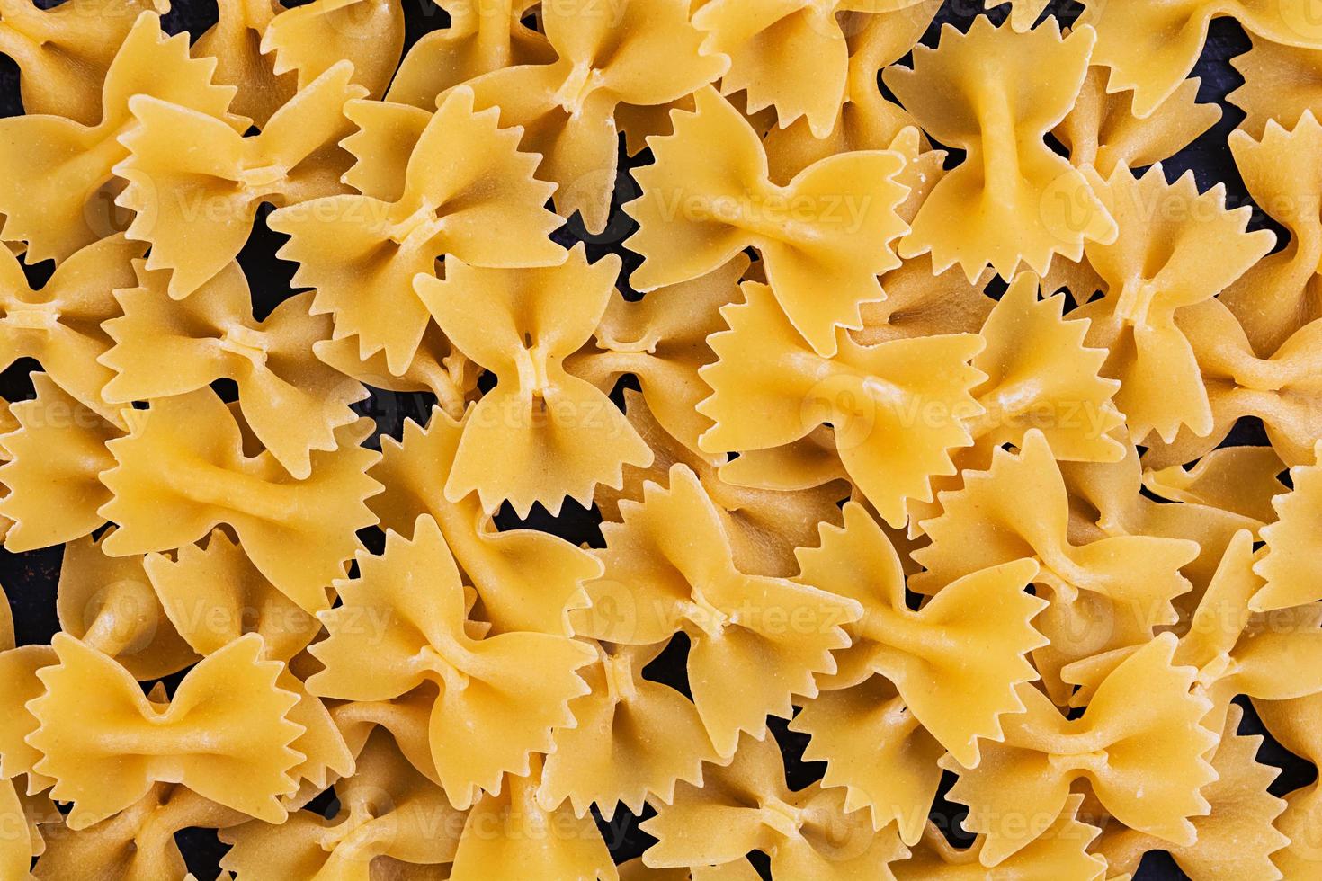 Dry pasta background. Close the raw farfalle pasta on dark background. Flat pattern. Top view. photo