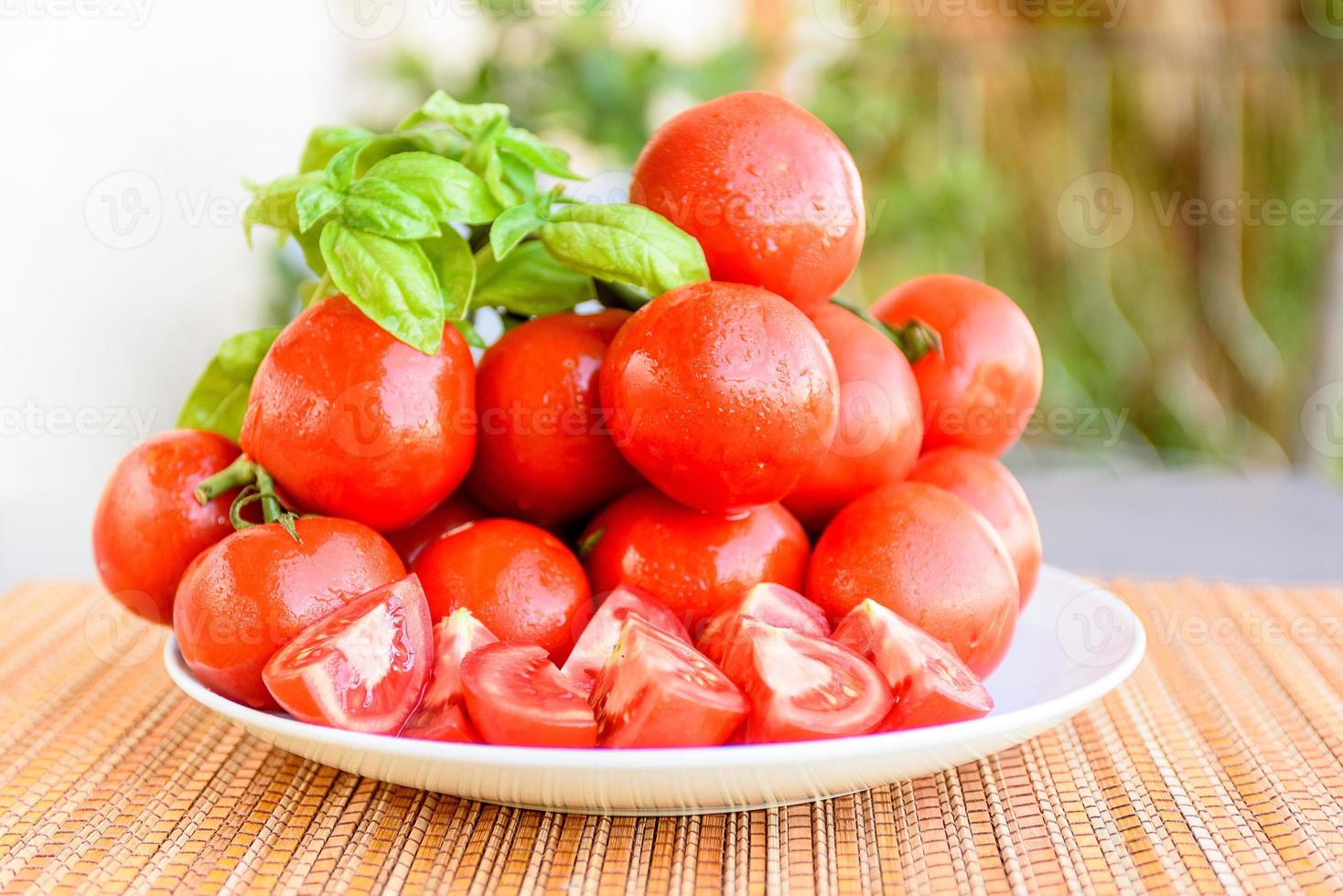 composición de tomates rojos y redondos en un plato blanco. con una ramita de albahaca foto