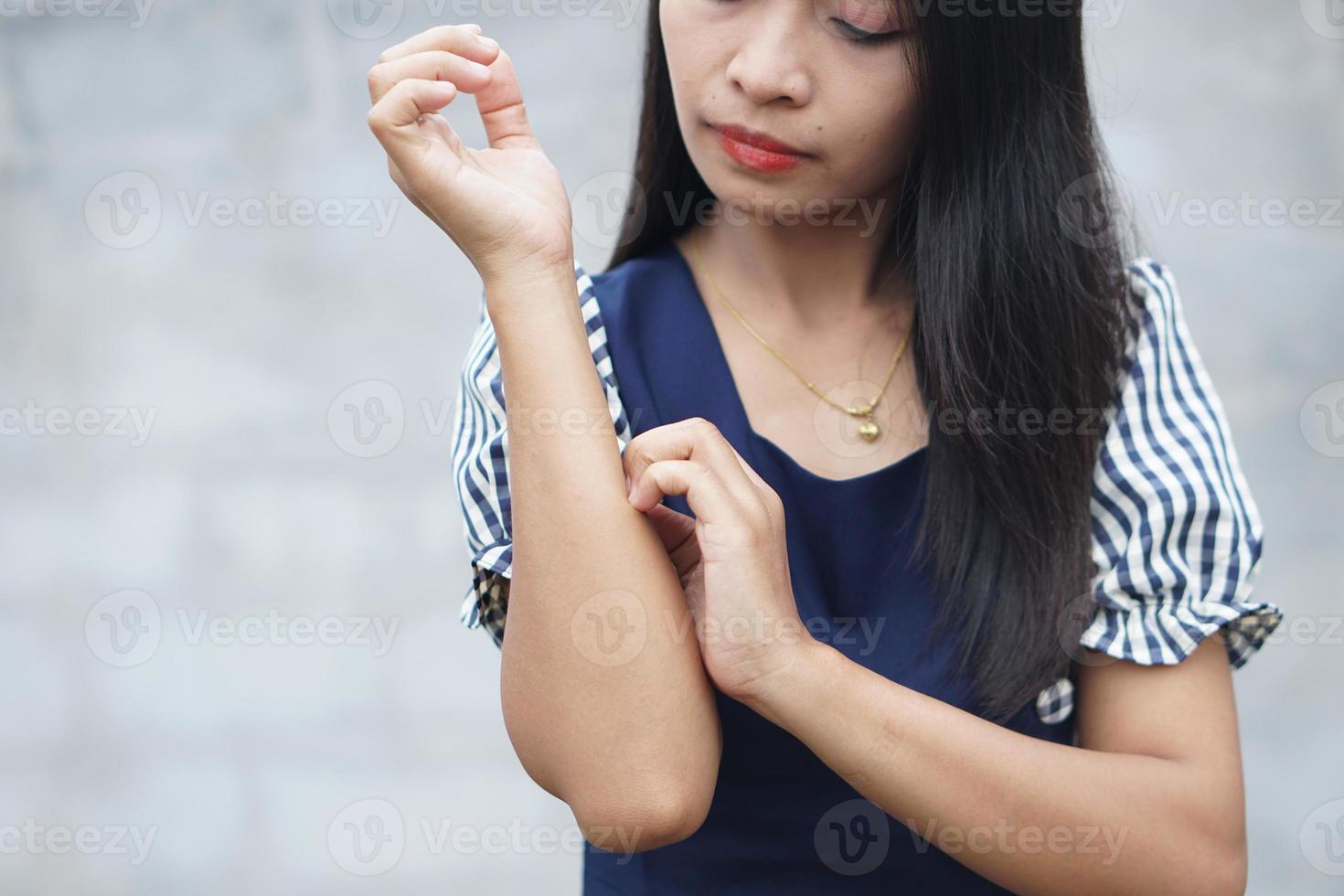 mujer rascándose el brazo por picazón en un fondo gris claro. la causa de la picazón en la piel incluye picaduras de insectos concepto de cuidado de la salud de la piel. foto