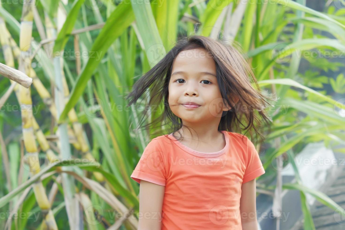 Happy expression Indonesian little girl with loose hair on sugar cane background photo