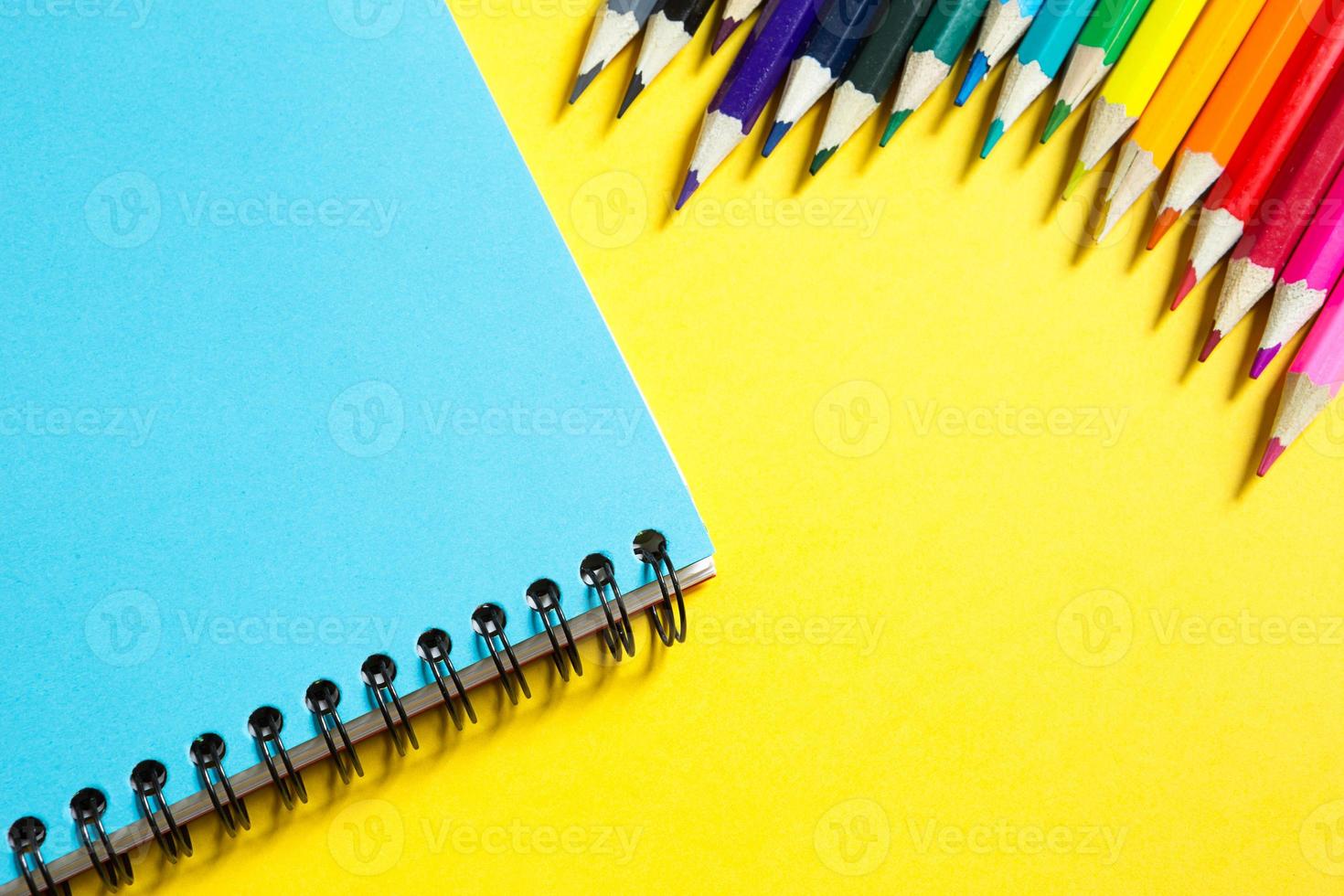 Rainbow palette of colored pencils with a spiral notebook on a yellow background,mock up, flat lay. Back to school, student recruitment, artist, drawing lessons. Copy space. Stationery for creativity photo