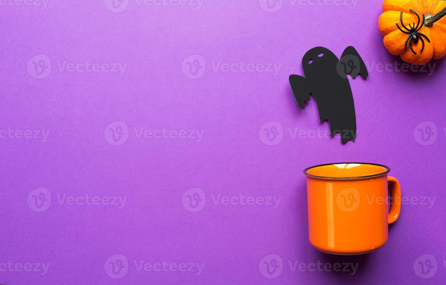 Orange mug on a purple background with terrible Halloween decorations. The concept of the Halloween holiday. Drink, fun, party. Copy space, mock up, flatly photo