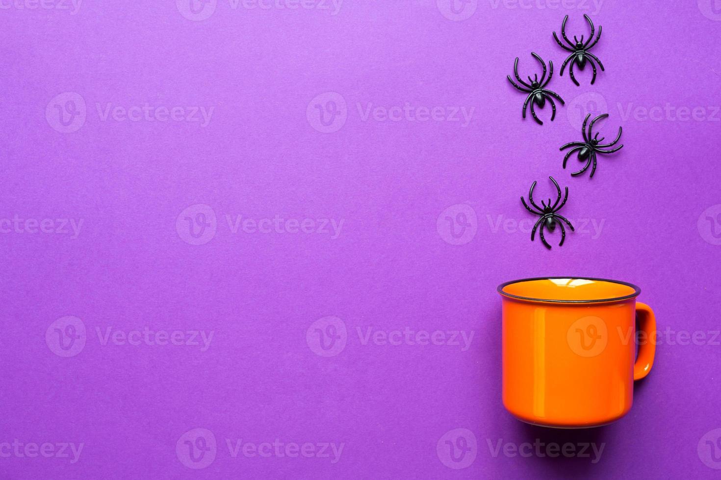 Orange mug on a purple background with spiders. The concept of the Halloween holiday. Terrible scenery, terrible drink, fun. Copy space, mock up, flatly photo