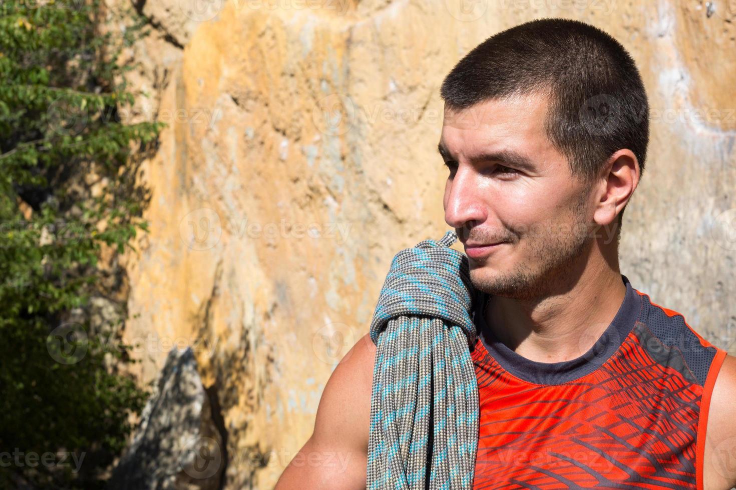 A male climber of Caucasian appearance with a coiled rope in his hand. Rope winding, knot, equipment storage. Hand in white magnesia. Red sports Jersey, extreme sports, rock climbing. Lifestyle photo