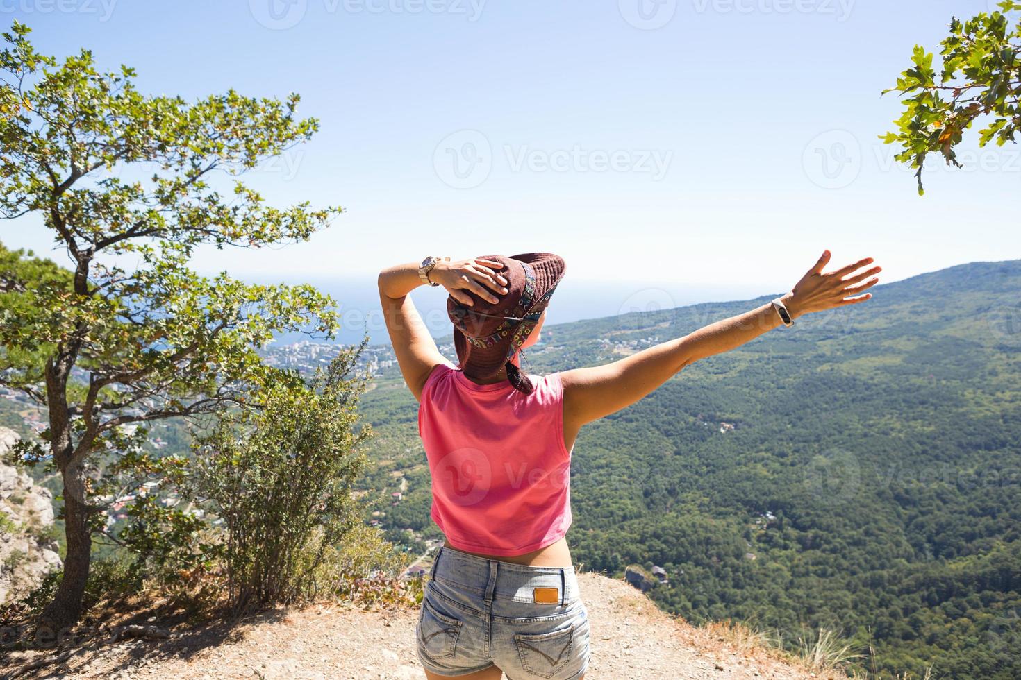 mujer turista con las manos levantadas mira la vista panorámica en la cima de la montaña y se regocija, disfruta de su libertad y aventura. trekking, viajes, ecoturismo activo, estilo de vida saludable, senderismo foto