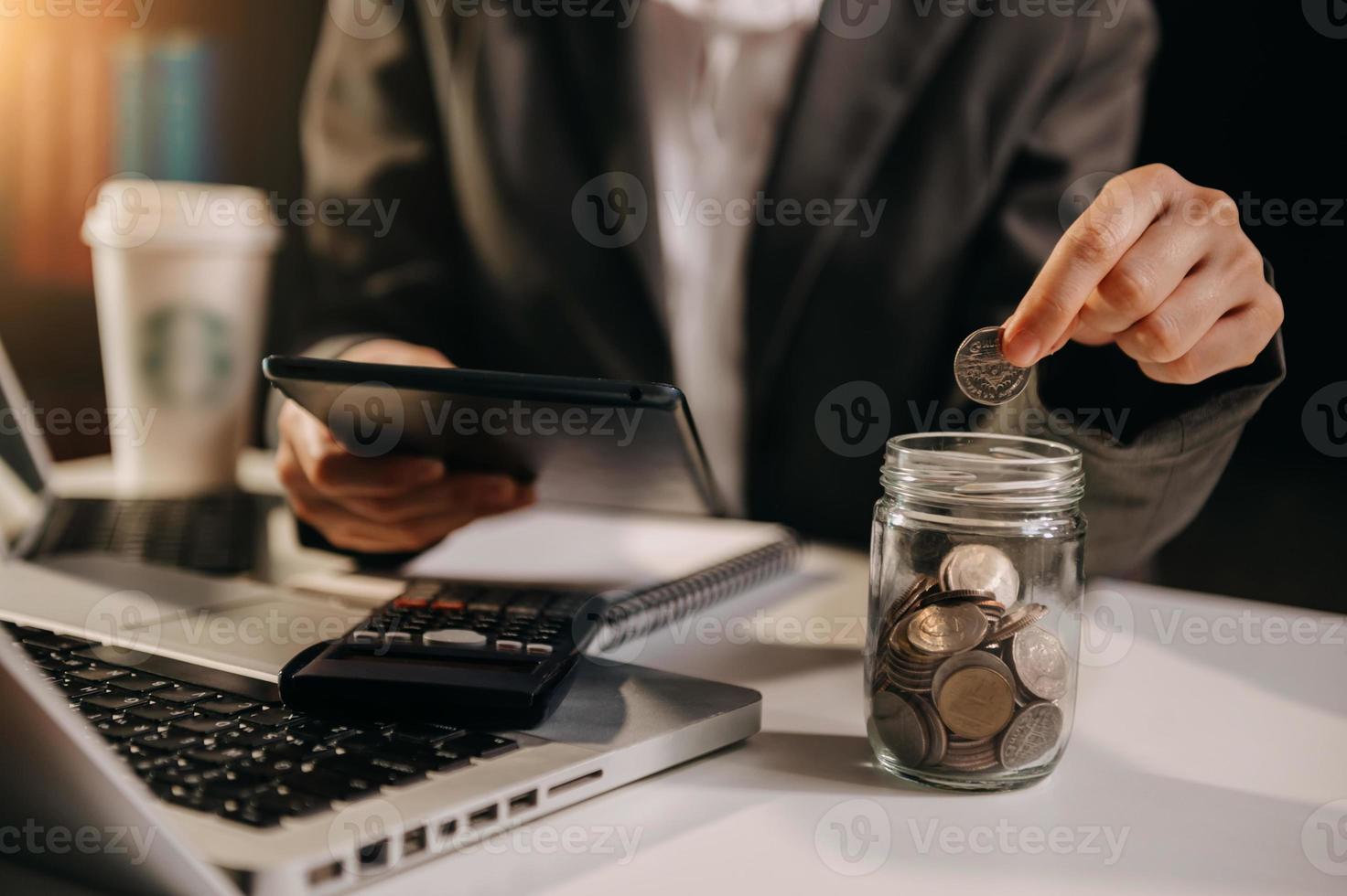 ahorrar dinero con la mano poniendo monedas en una jarra y una calculadora para calcular el concepto de presupuesto finanzas y contabilidad foto