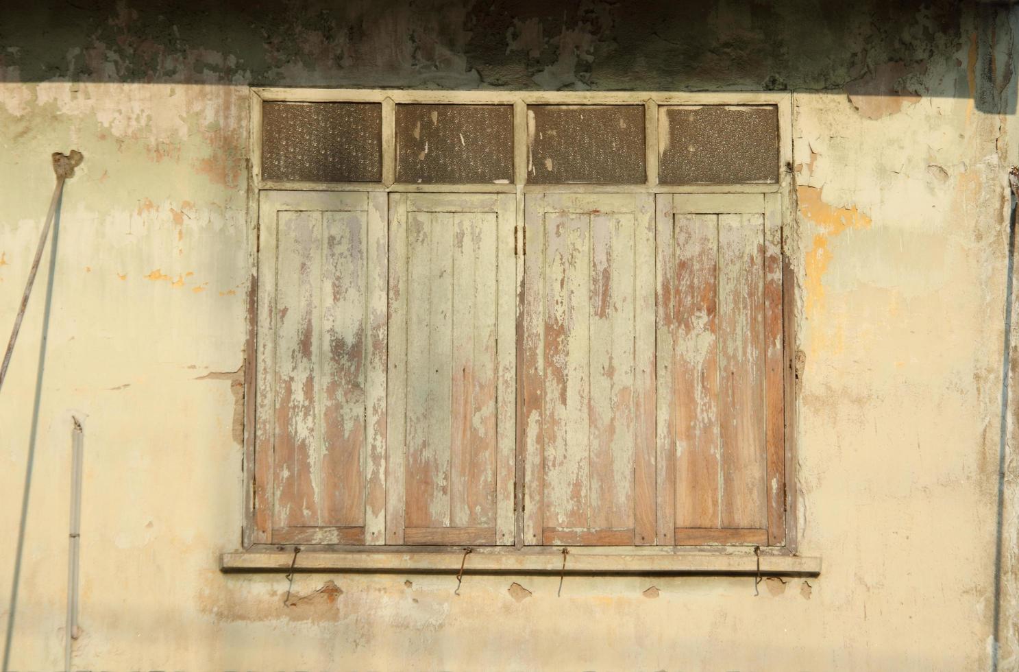 Painted wood window on light yellow painted wall of retro style building, color flake off surface of closed window and building. photo