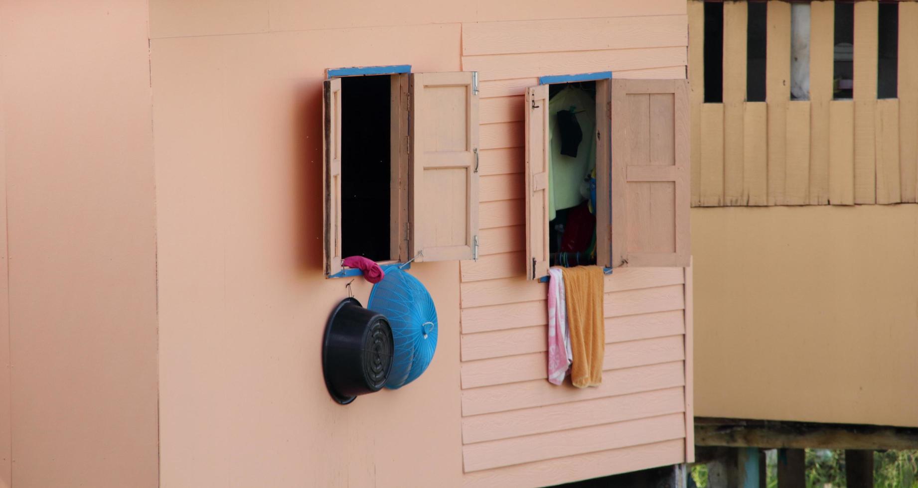 Old window open on light brown and smooth surface wall, plastic bowl and towel are hanging on. Retro style window of wood house in Thailand. Beside view. photo