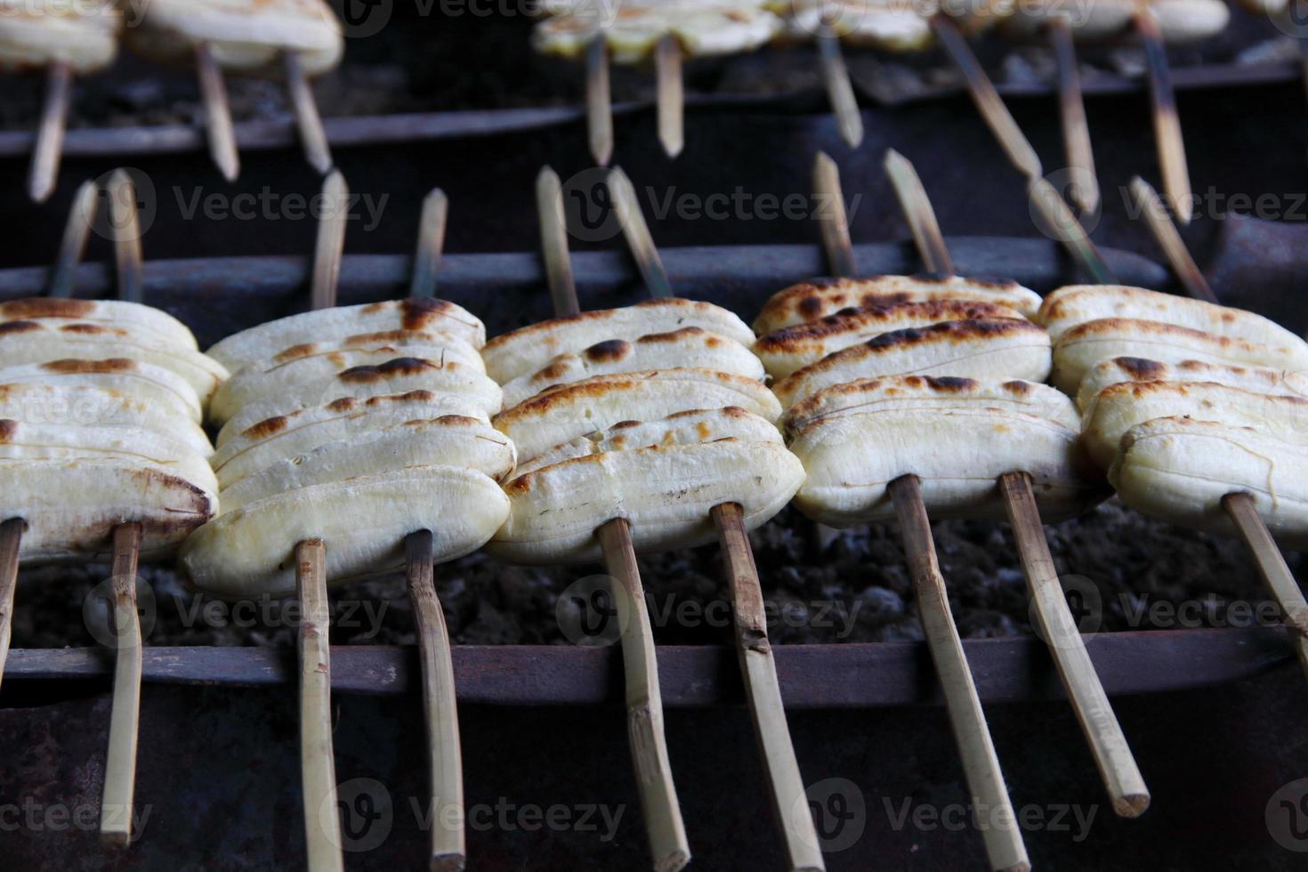 Bananas are on bamboo skewer. Row of bananas are roasting on fire, Thailand. photo