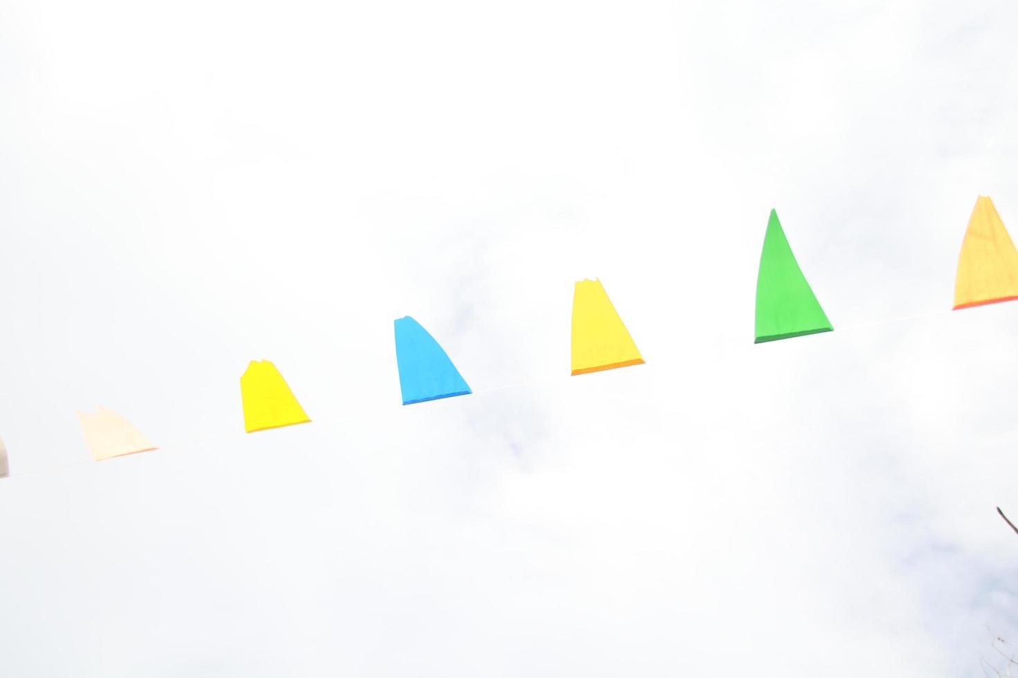 Yellow, blue, green flags in triangle shape are on thread and white sky background. photo