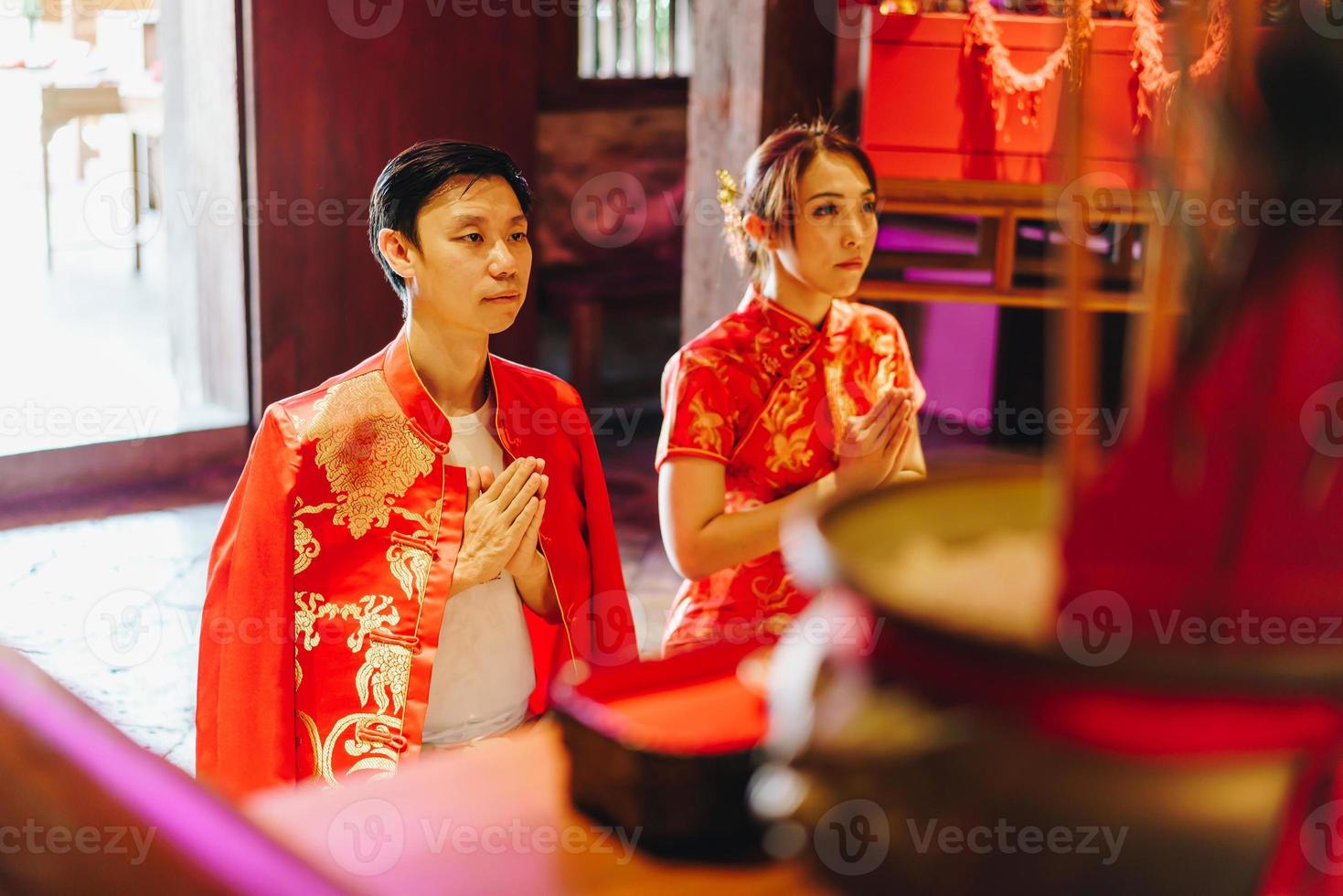 feliz joven pareja asiática con vestidos tradicionales chinos rezando en el templo foto