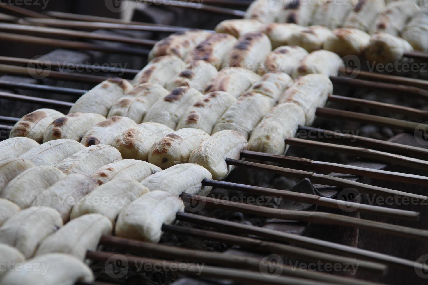 Bananas are on bamboo skewer. Row of bananas are roasting on fire, Thailand. photo