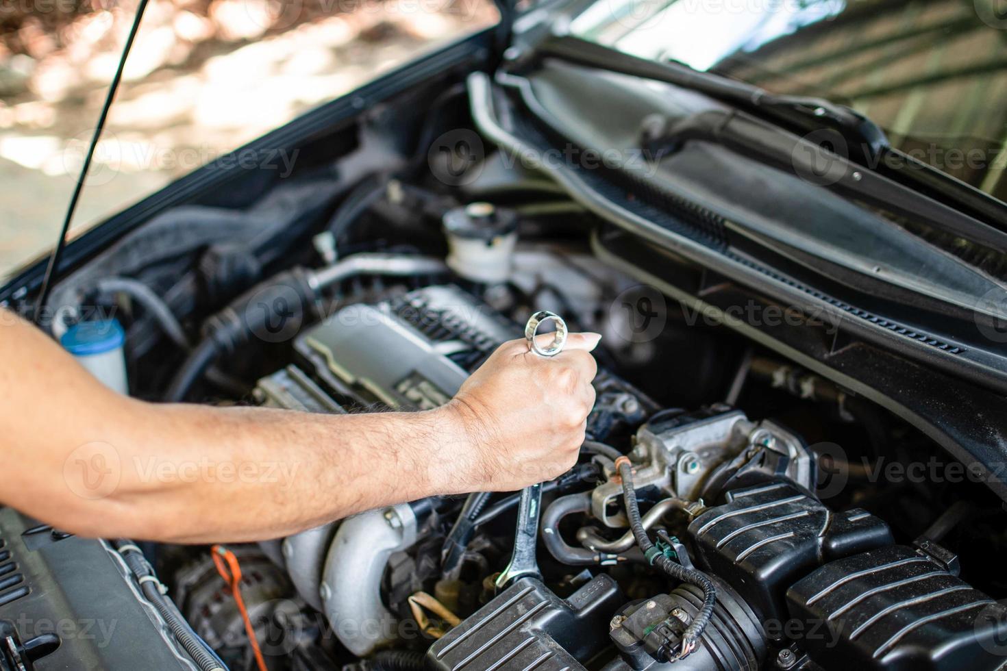 concepto de mantenimiento del motor. los mecánicos sostienen una llave para apretar los pernos en las reparaciones del motor. coche negro, motor apagado. los ingenieros están comprobando el sistema de combustión de los cilindros. fondo borroso foto