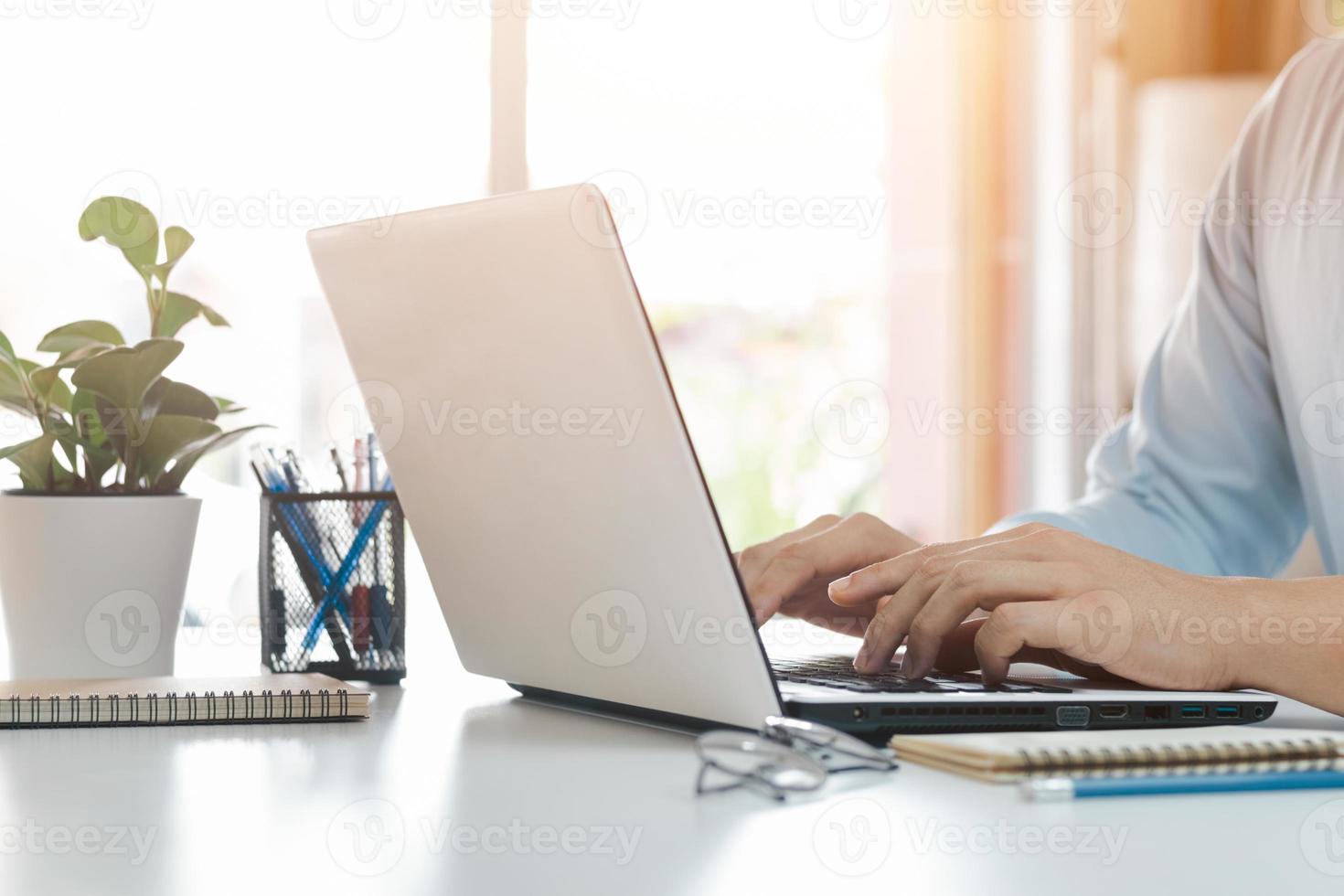 young man using laptop computer and mobile phone When looking for financial information in business, work at the desk. Writing with a pen, studying remotely from home and working from home. photo