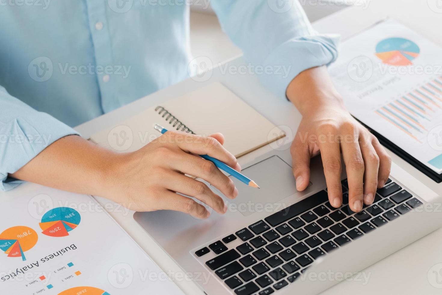 young man using laptop computer and mobile phone When looking for financial information in business, work at the desk. Writing with a pen, studying remotely from home and working from home. photo