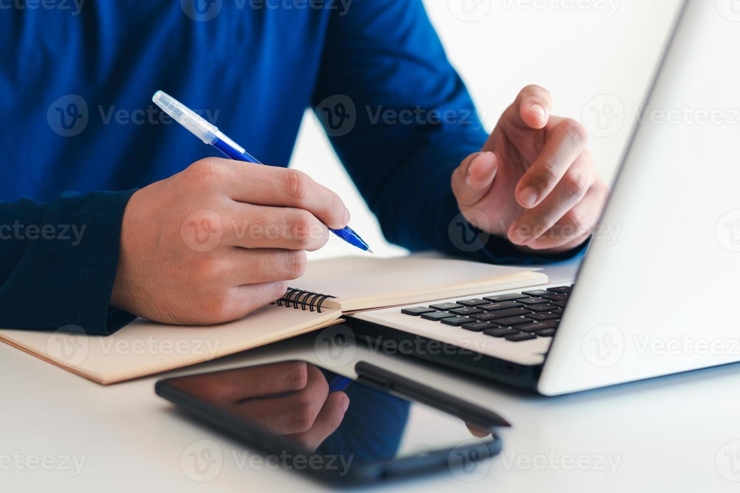 el hombre de negocios tomando notas resume la reunión en línea con una computadora portátil, trabajando solo, sentado en su escritorio. trabajando desde casa, manos de primer plano. foto