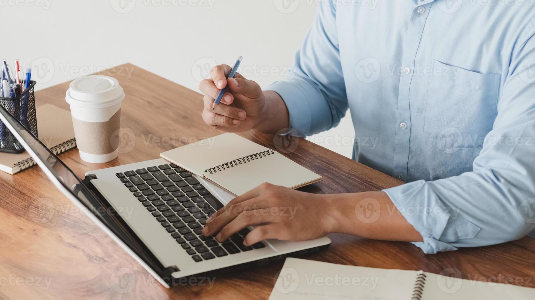 young man using laptop computer and mobile phone When looking for financial information in business, work at the desk. Writing with a pen, studying remotely from home and working from home. photo