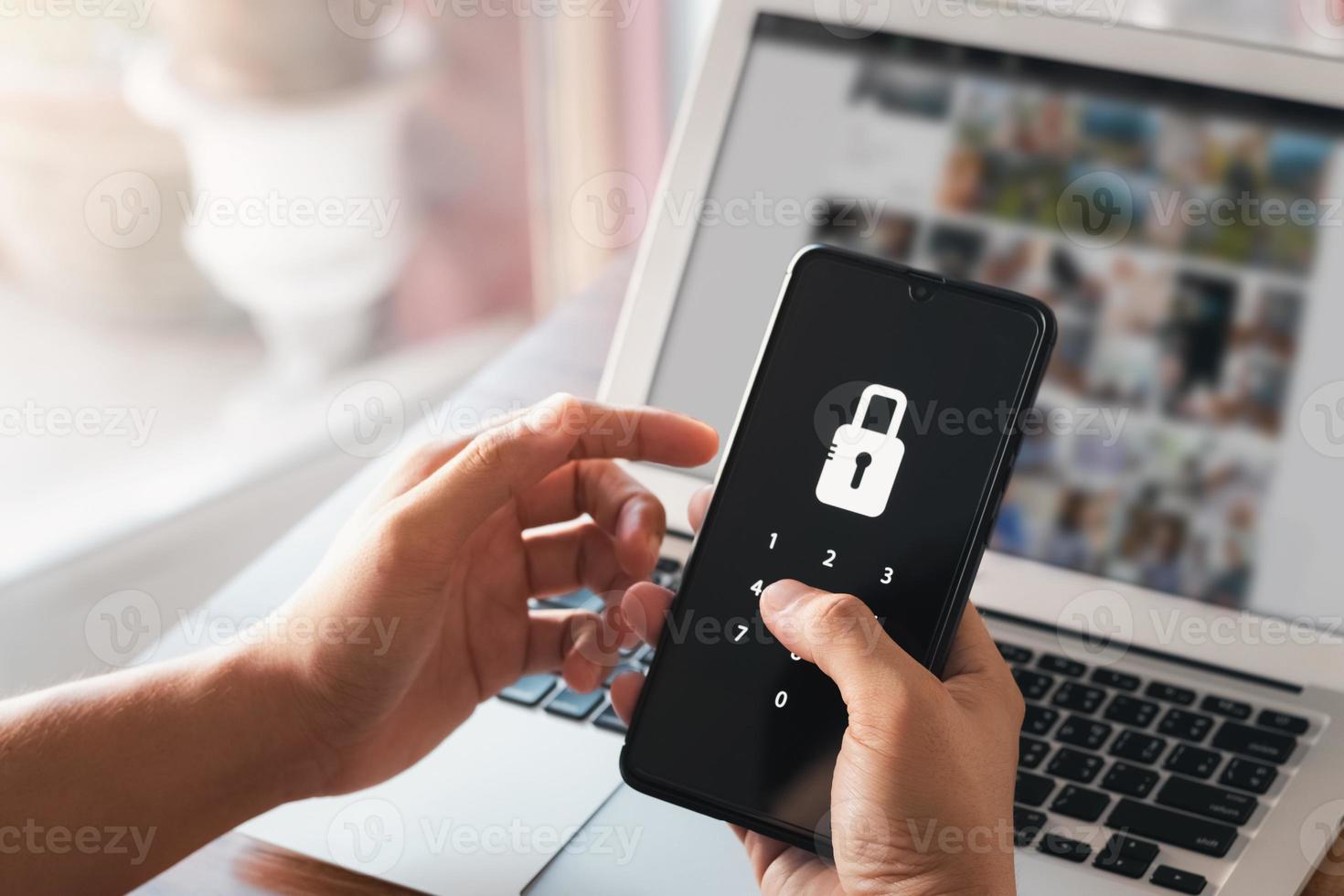 Hacking a Phishing mobile phone with a password to access a smartphone, security threats online, and fraud. A young man with a cell phone and laptop is secure in his bank account. photo