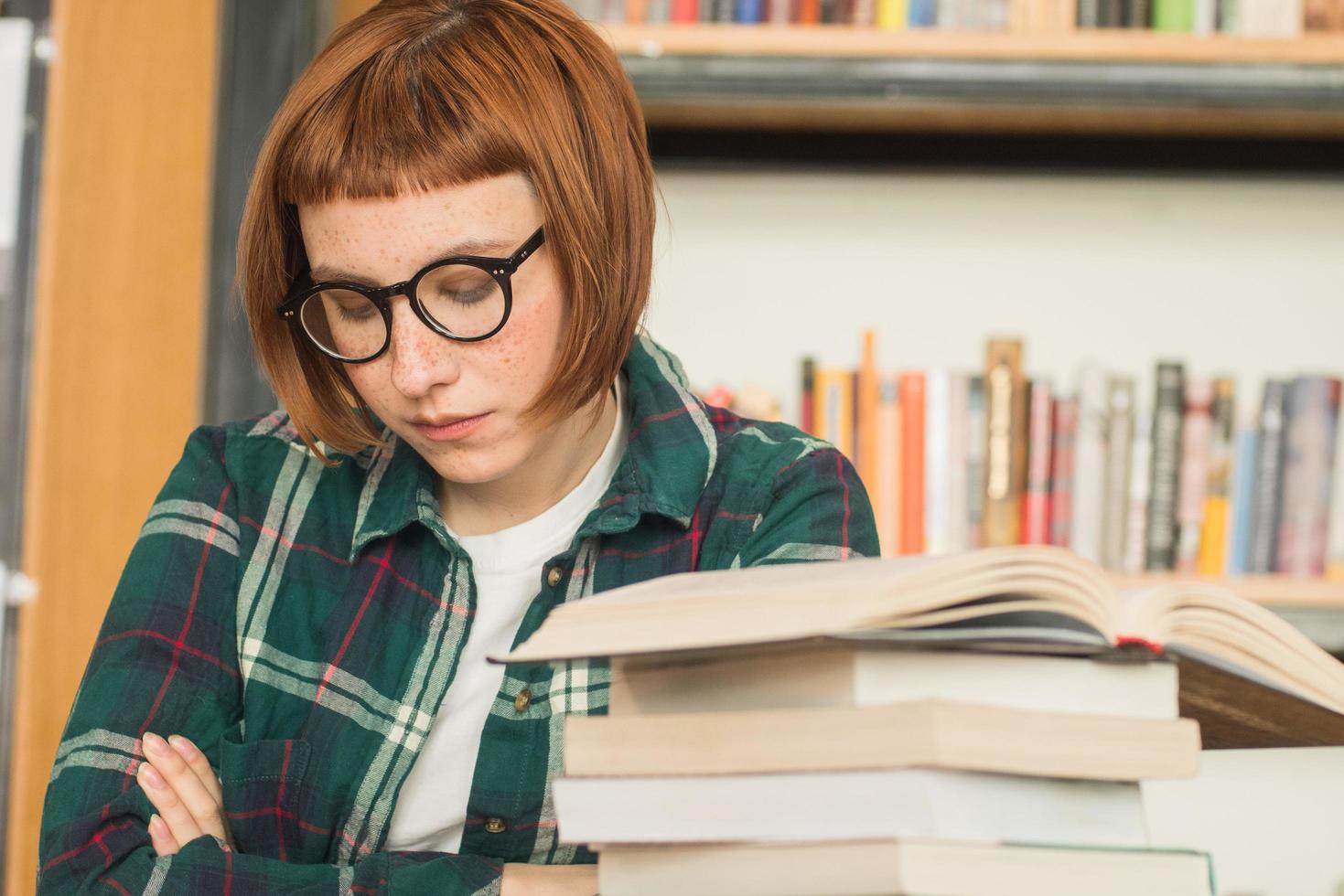 Young redhead woman in glasses read book in the library photo