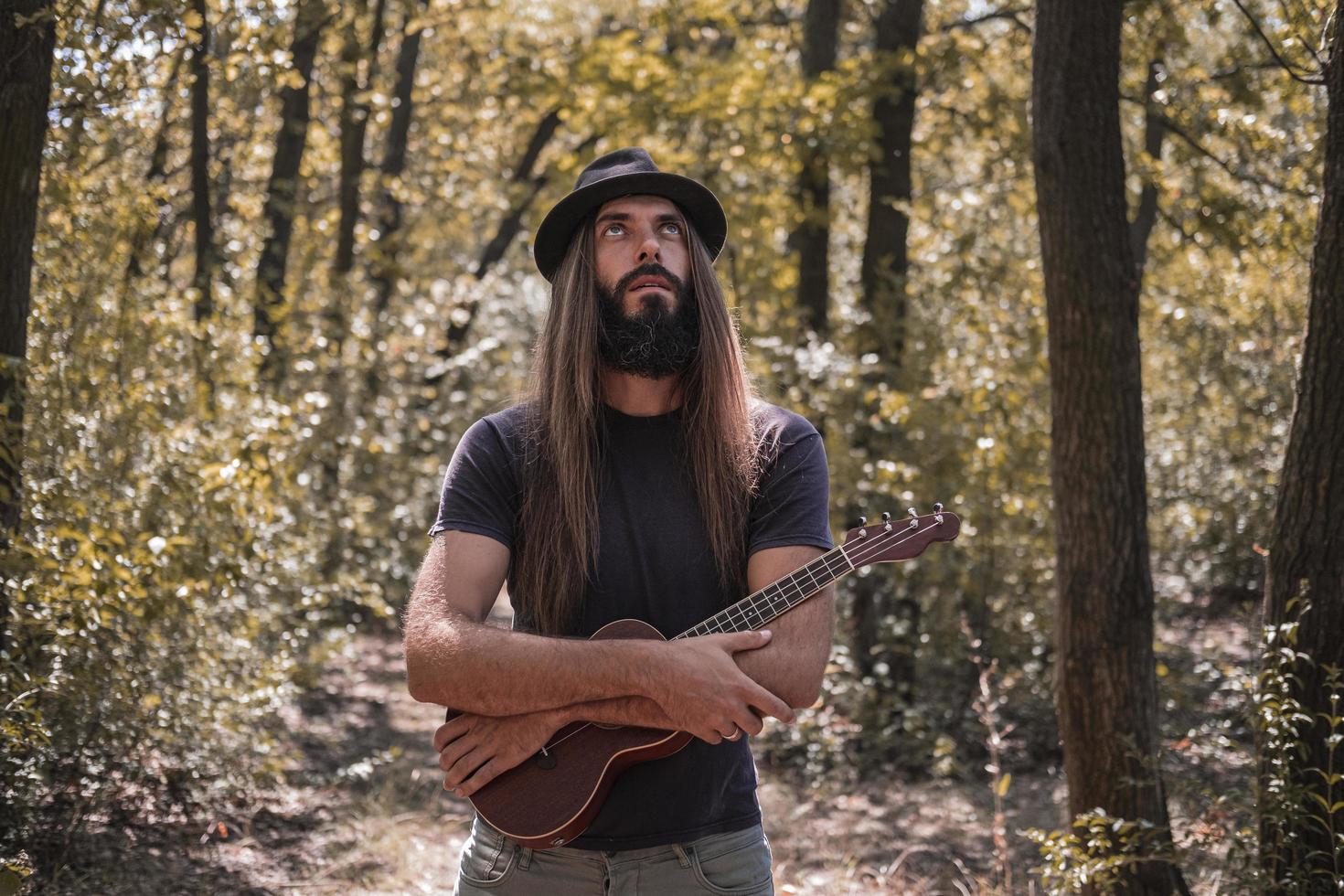 Bearded male with longhait and hat posing with ukulele in the forest photo