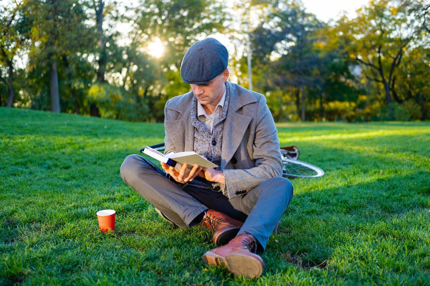 joven hipster masculino lee un libro en el parque de otoño foto