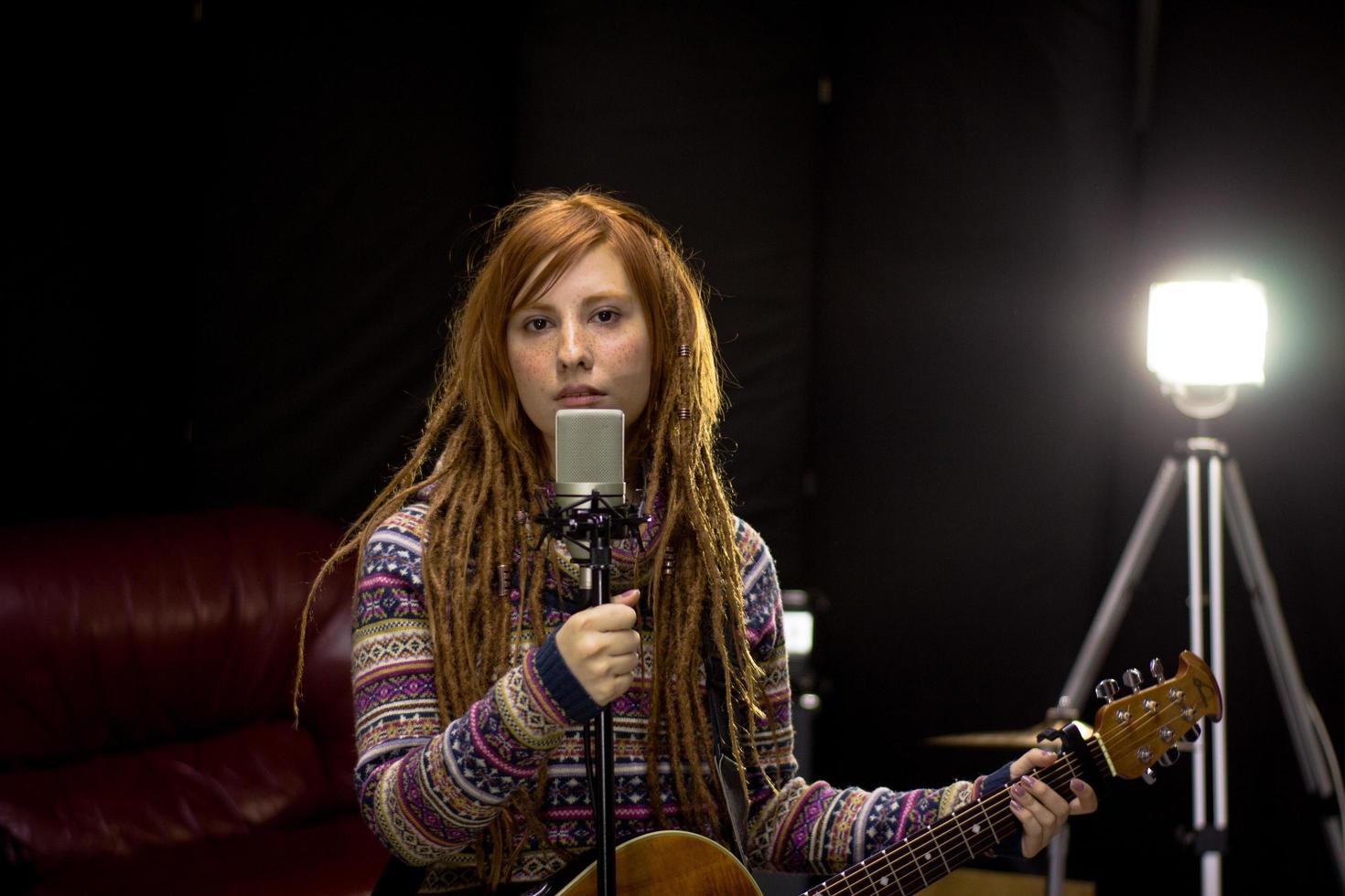 mujer joven con guitarra canta en el estudio foto