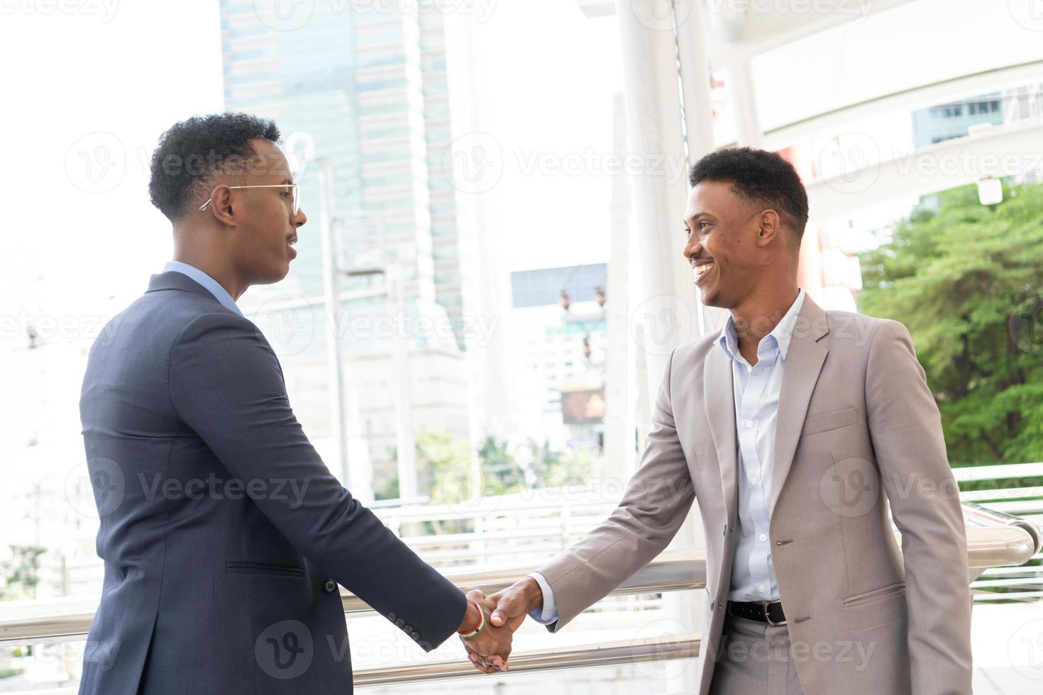 bienvenido a nuestro equipo. jóvenes modernos con ropa informal elegante dándose la mano. dos hombres de negocios sonrientes dándose la mano. dos hombres de negocios confiados dándose la mano en el exterior de la oficina. foto