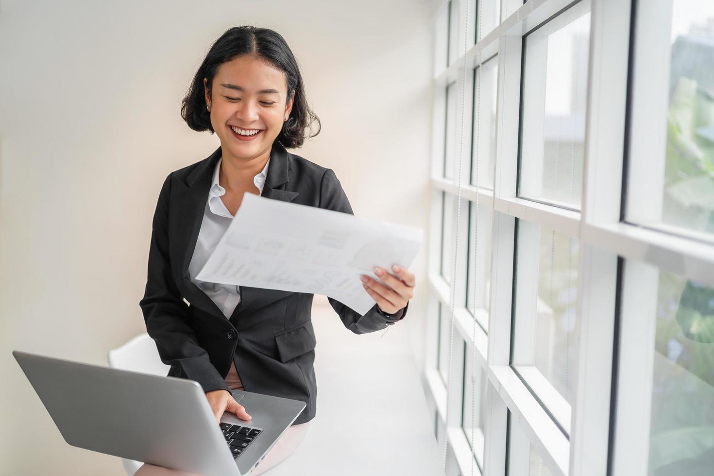 business woman smiling with holding paper and using laptop in office photo