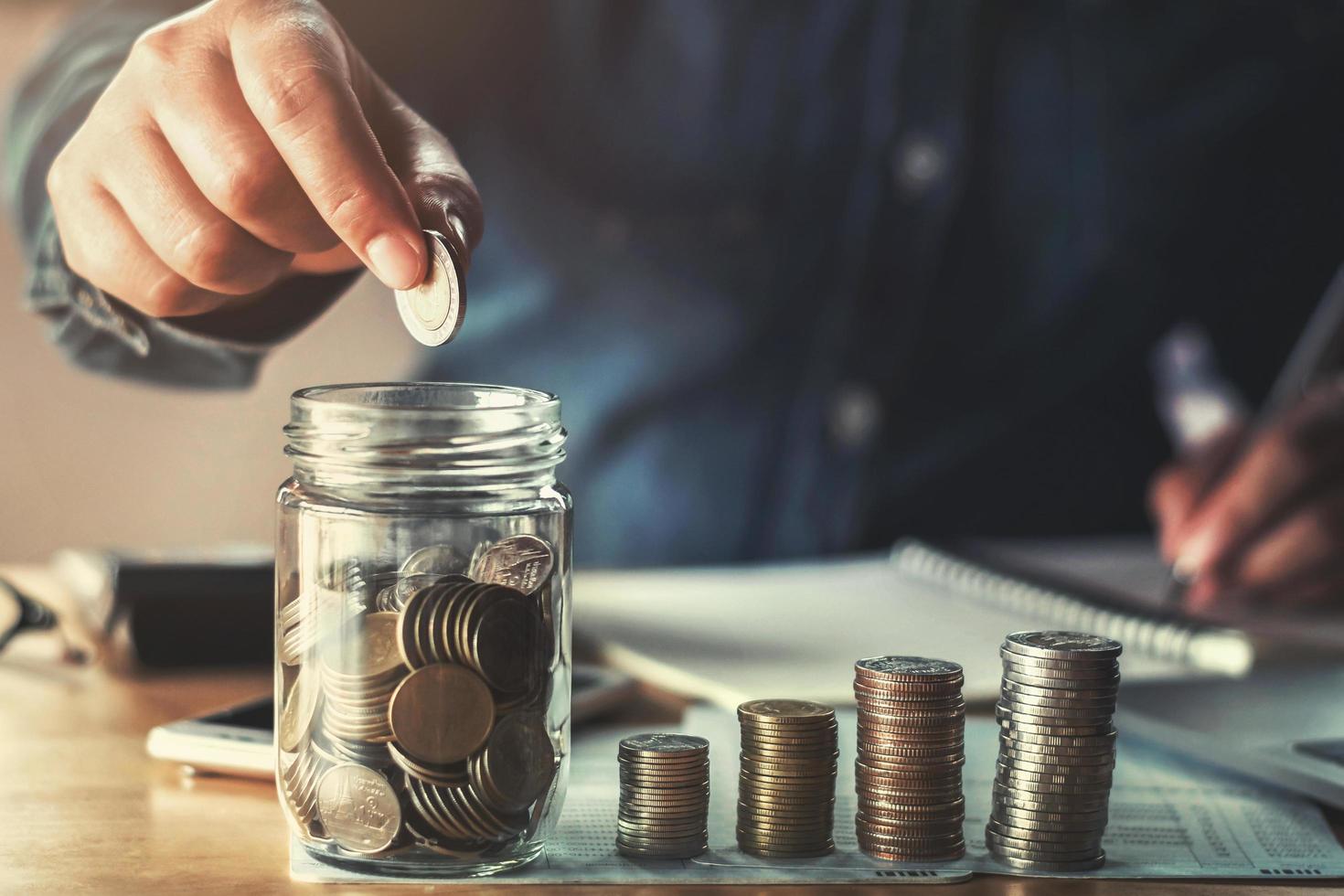 ahorrar dinero con la mano poniendo monedas en una jarra de vidrio concepto financiero foto