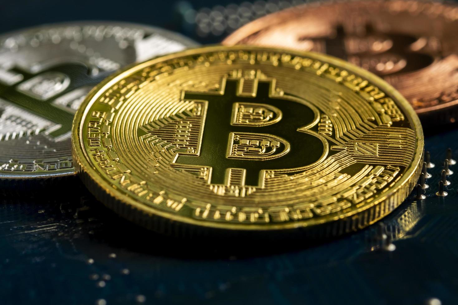 Macro view of gold, silver and bronze color shiny coins with bitcoin symbol on a mainboard. photo