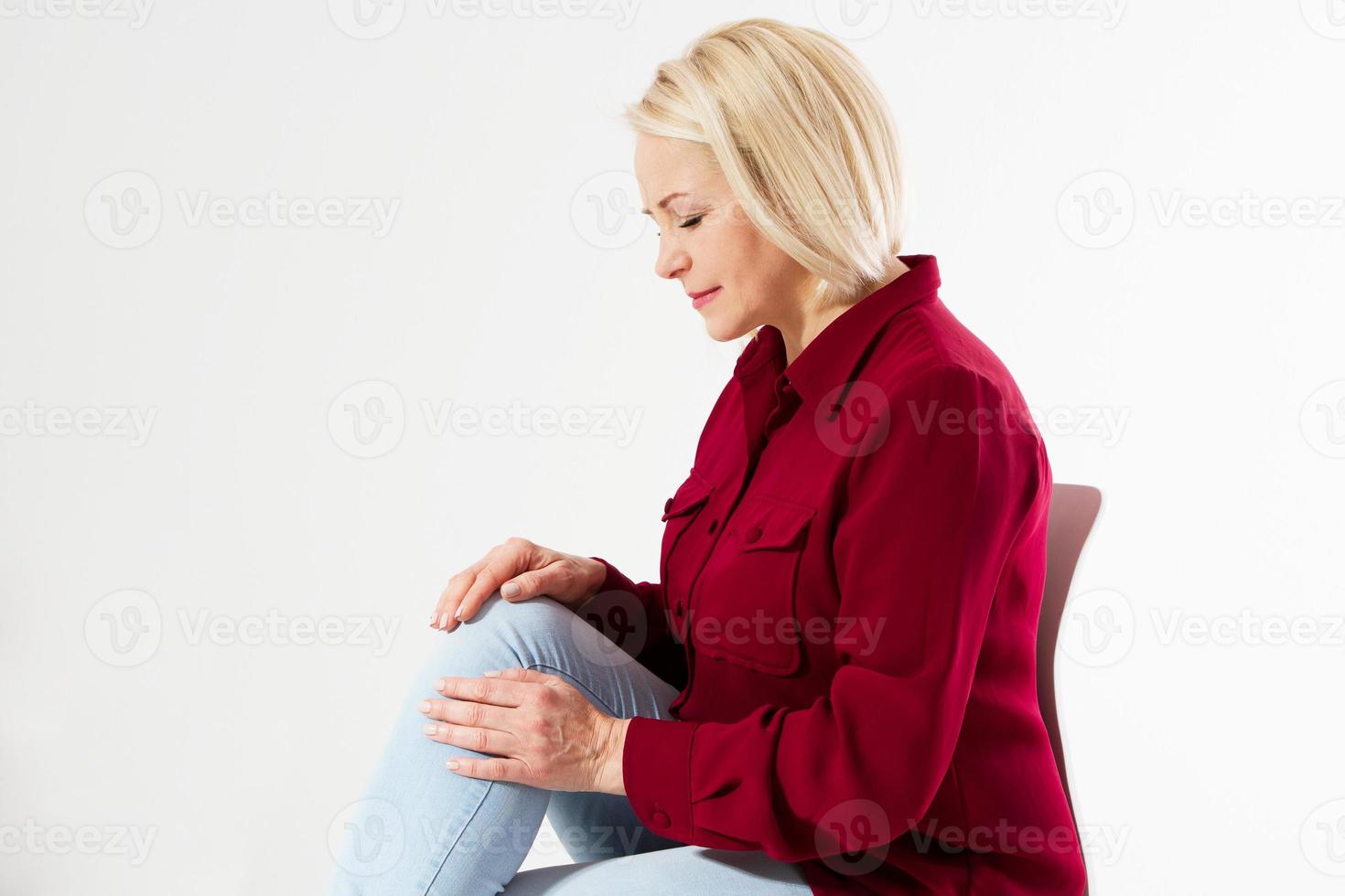 Joint pain, blonde woman touching leg injury isolated on white background, female rheumatism, woman sittin on chair and touching knee pain photo