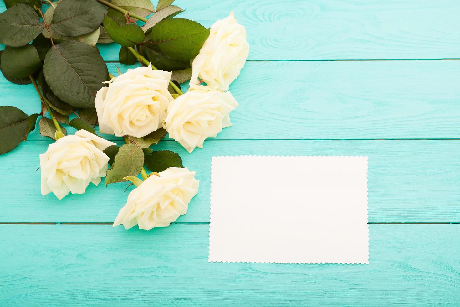 marco de rosas coloridas sobre fondo de madera azul con tarjeta de papel y espacio de copia. vista superior y enfoque selectivo. Bosquejo foto