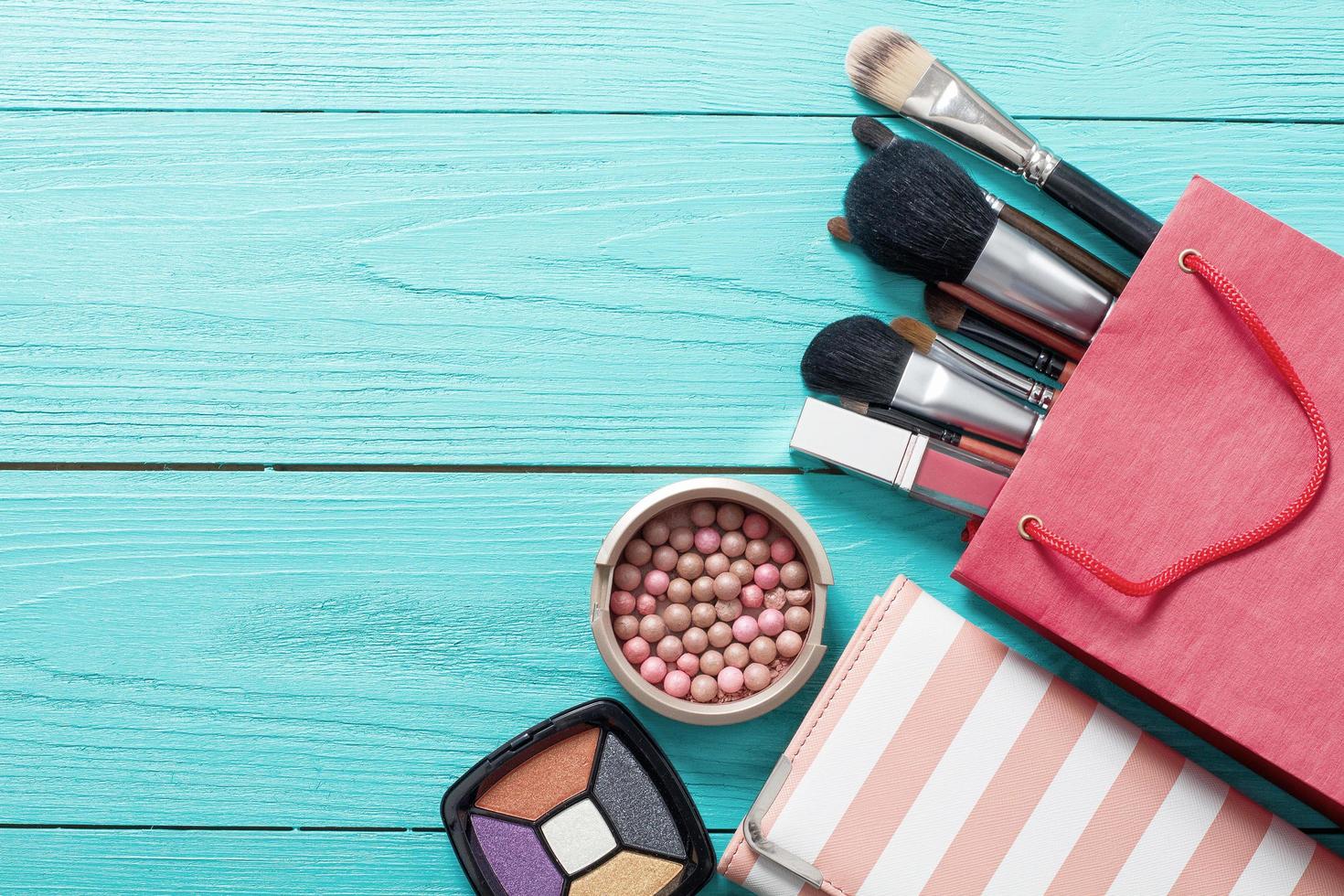 Frame of makeup products and accessories with red bag on blue wooden background. Top view and mock up. photo