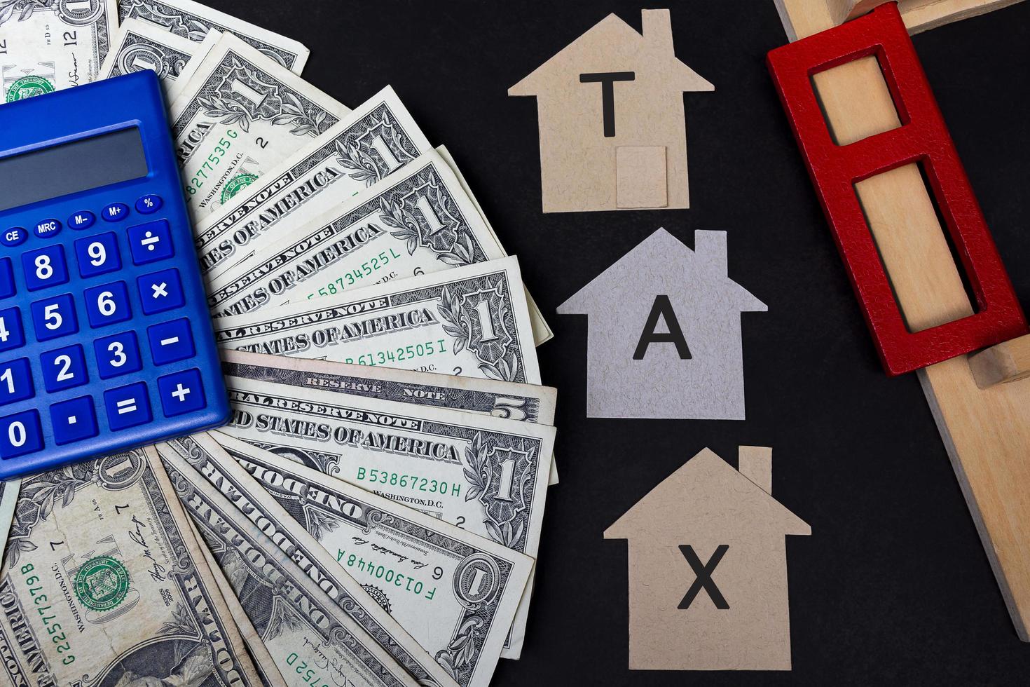 Tax text on brown paper house model with dollar banknotes, blue calculator and window frame on dark wooden table. Concept for real estate property tax. photo