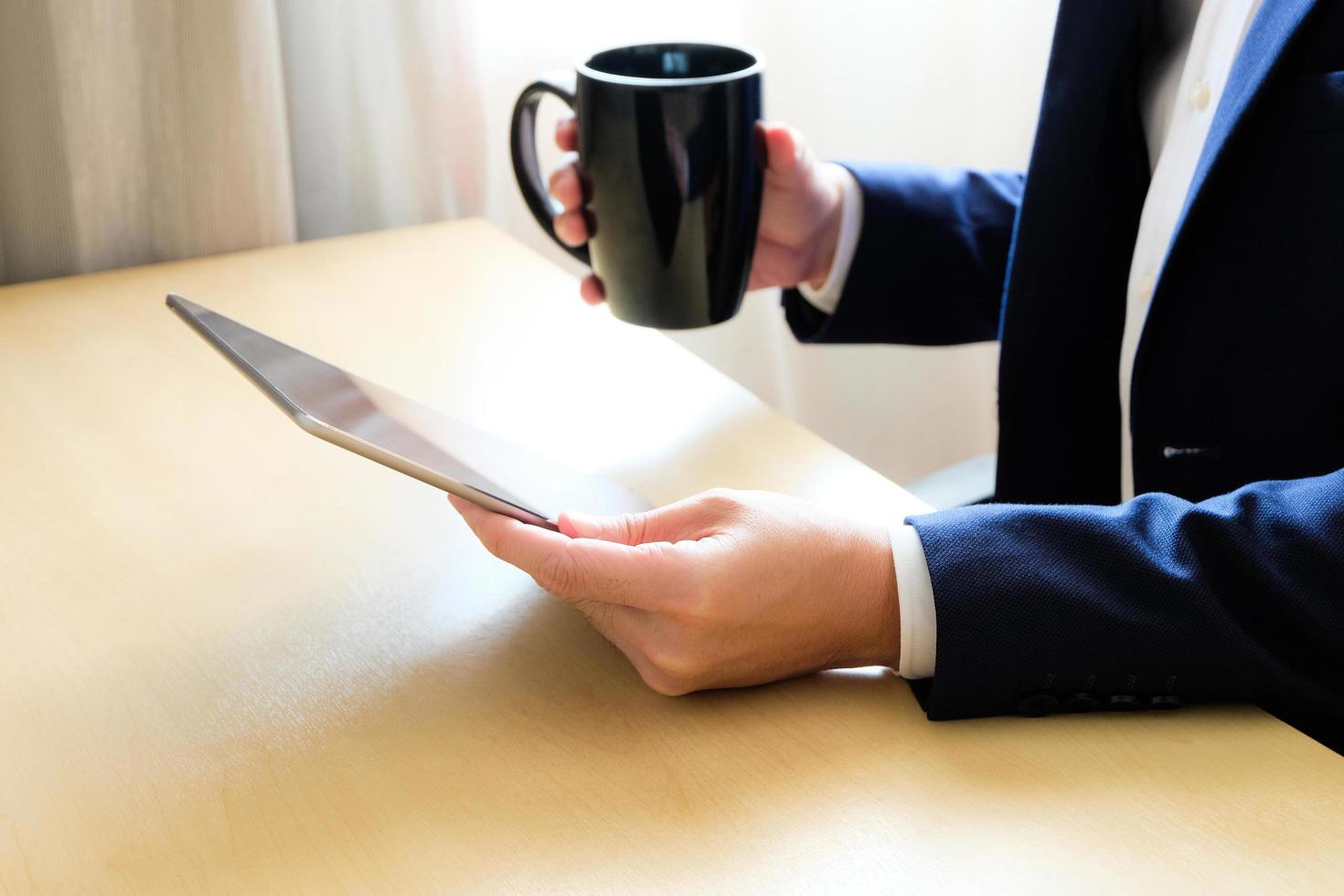 Man business person with suit using tablet device reading news or check for financial stock exchange information while drinking coffee in the morning at the cafe or office. with copy space for text photo