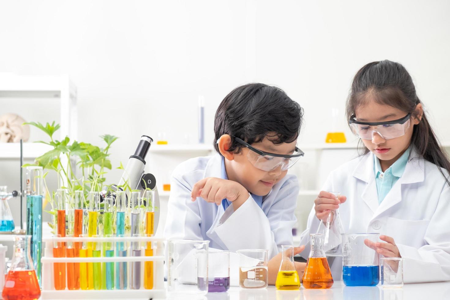 Young Asian boy and girl smile and having fun while learning science experiment in laboratory with teacher in classroom. Study with scientific equipment and tubes. Education concept. photo