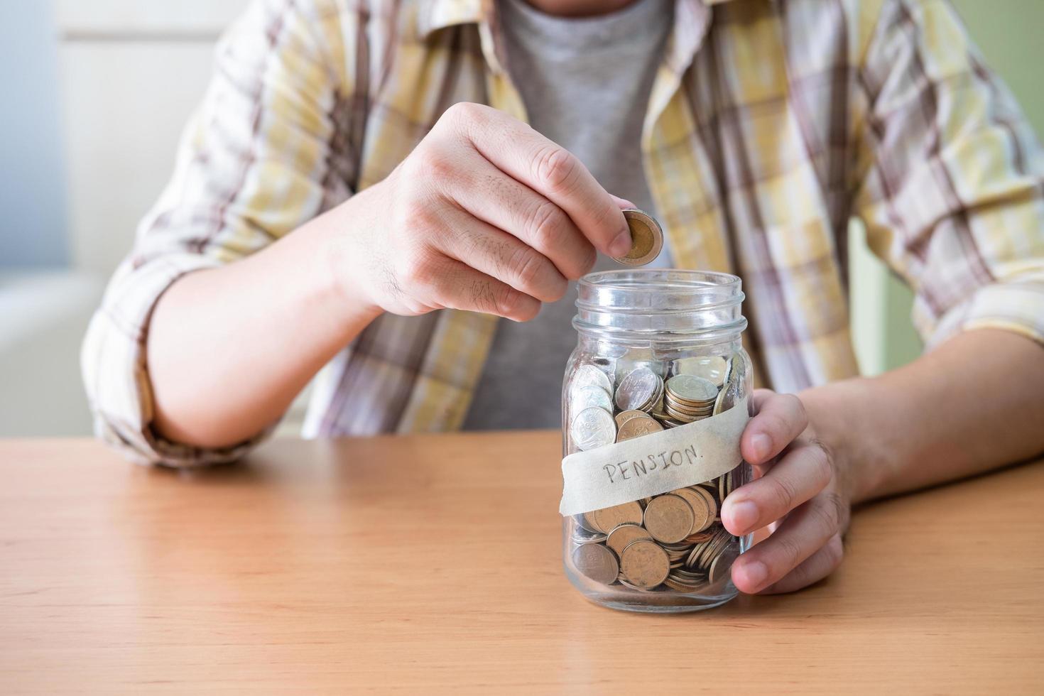 enfoque selectivo en el frasco de vidrio. los hombres ponen a mano monedas en un frasco de vidrio lleno de ahorro de monedas para el fondo de pensiones de jubilación. primer plano interior con tela informal. foto