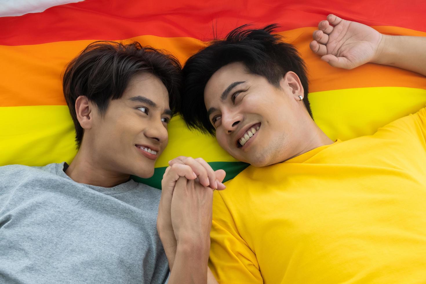 Asian gay homosexual couple holding hands on the bed.  With rainbow flag as LGBT sign at the background. Gender equality and right concept, playful and romantic moment. photo
