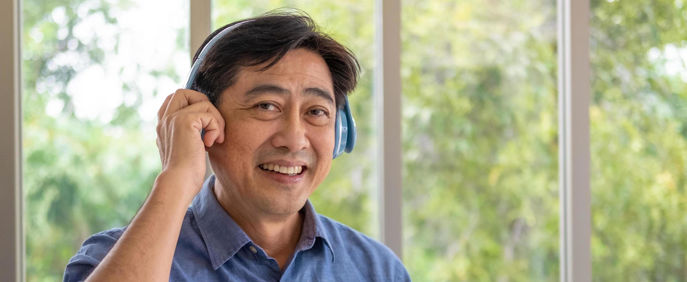 Banner, panorama shot of senior Asian grandfather enjoy and feeling happy while listening music from wireless headphone that streaming music from smartphone or tablet device. Elderly lifestyle. photo