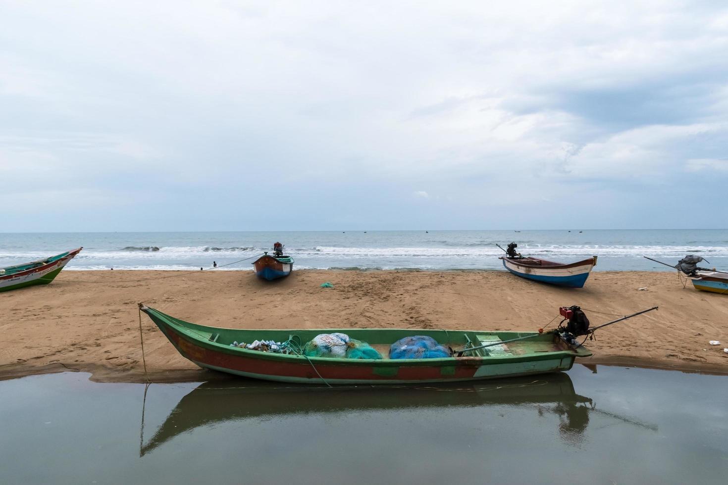 un barco de pesca de madera verde junto a un charco de agua en una playa de mahabalipuram. foto