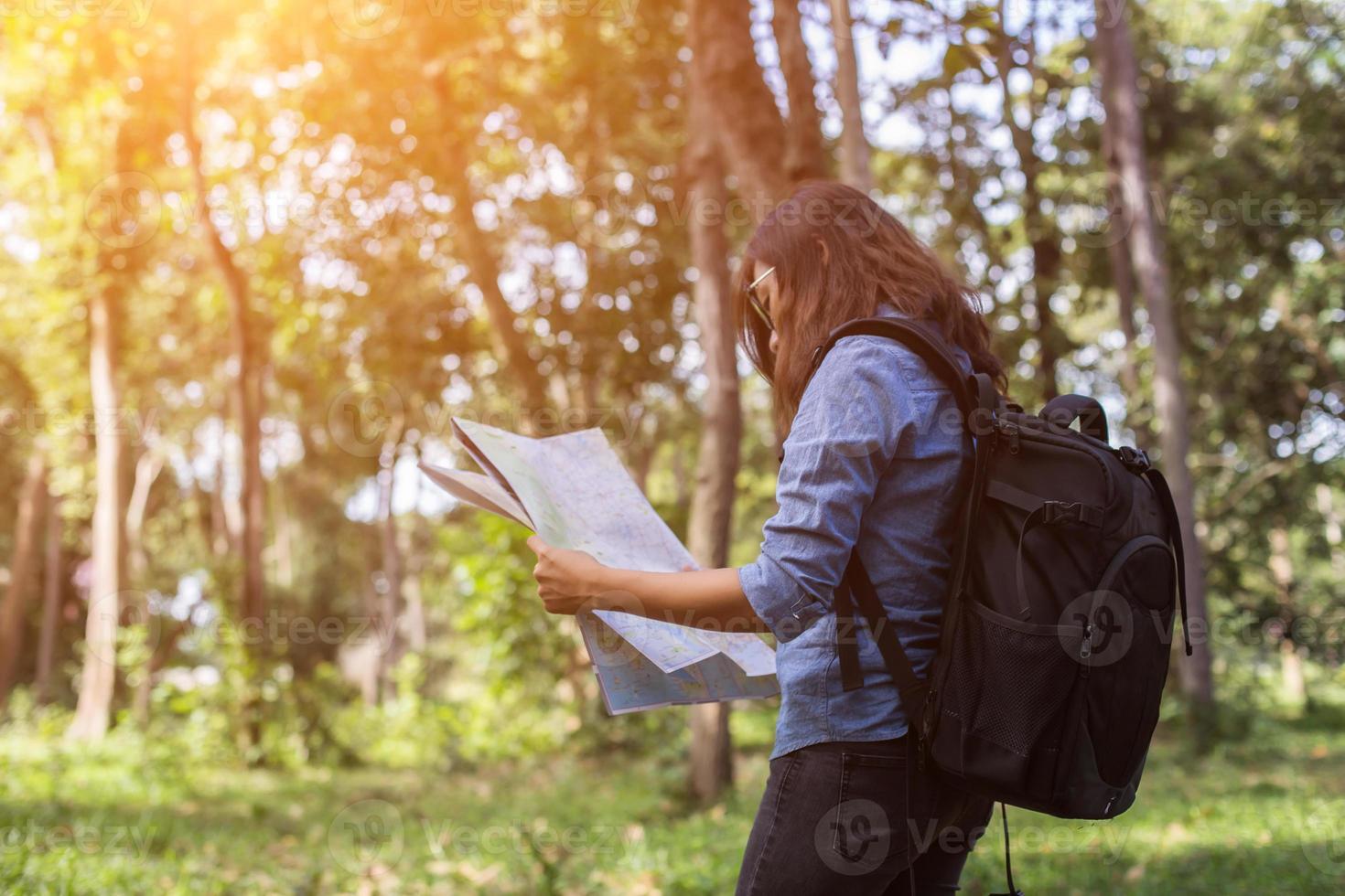 mujer excursionista con mochila revisa el mapa para encontrar direcciones en el área silvestre foto
