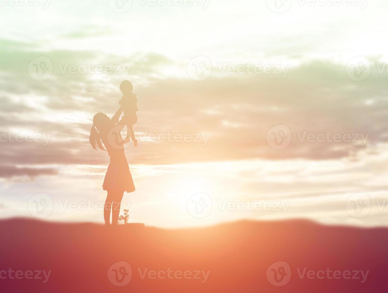 una silueta de una niña feliz los brazos de su madre amorosa para un abrazo, frente a la puesta de sol en el cielo en un día de verano. foto