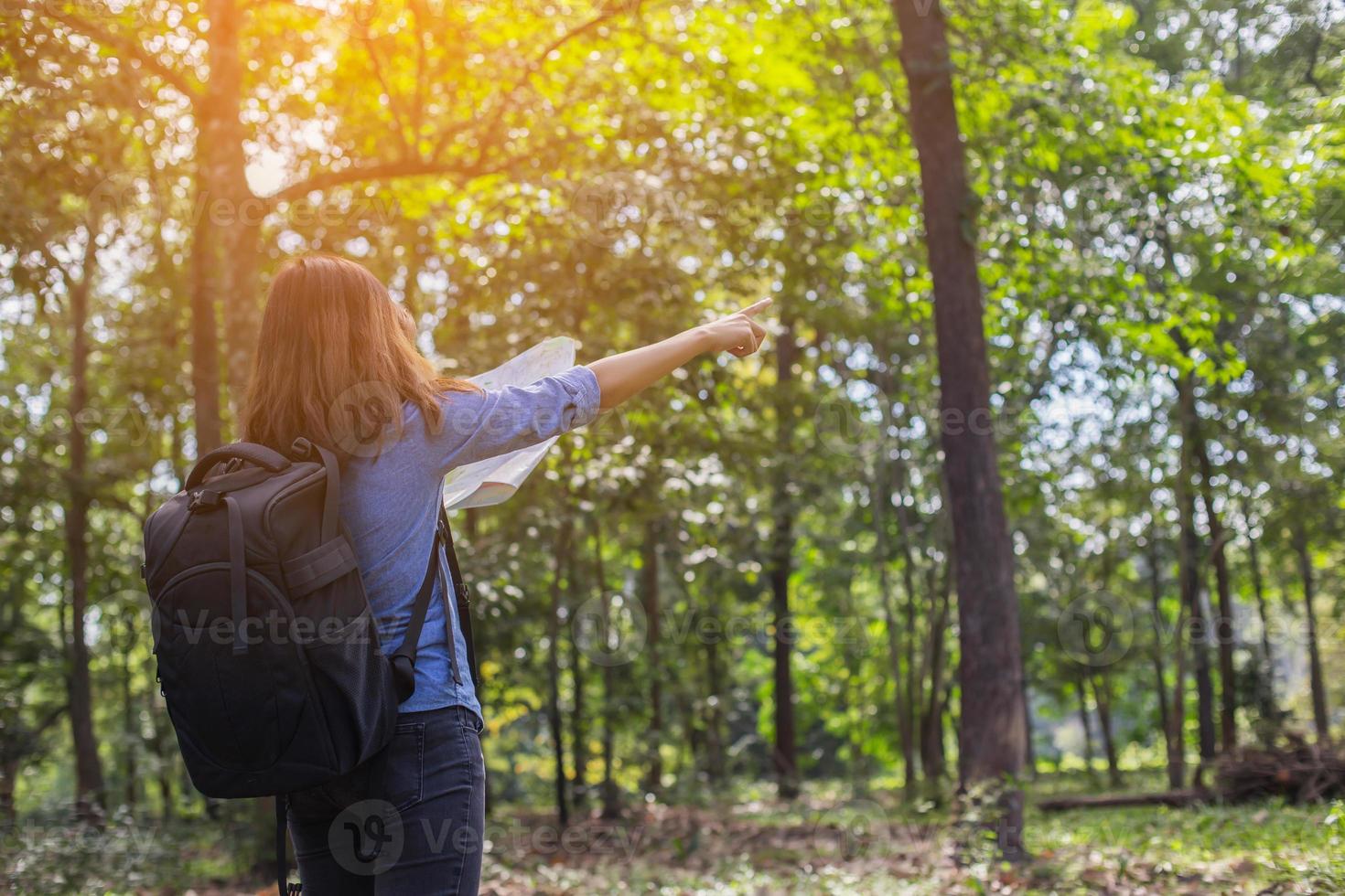 mujer excursionista con mochila revisa el mapa para encontrar direcciones en el área silvestre foto