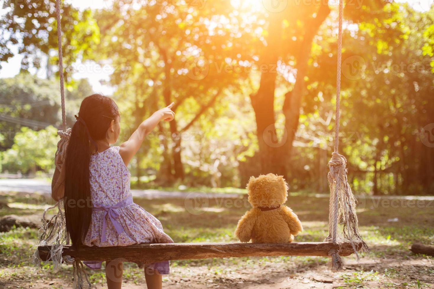 A little girl and teddy bear sitting on a swing. photo