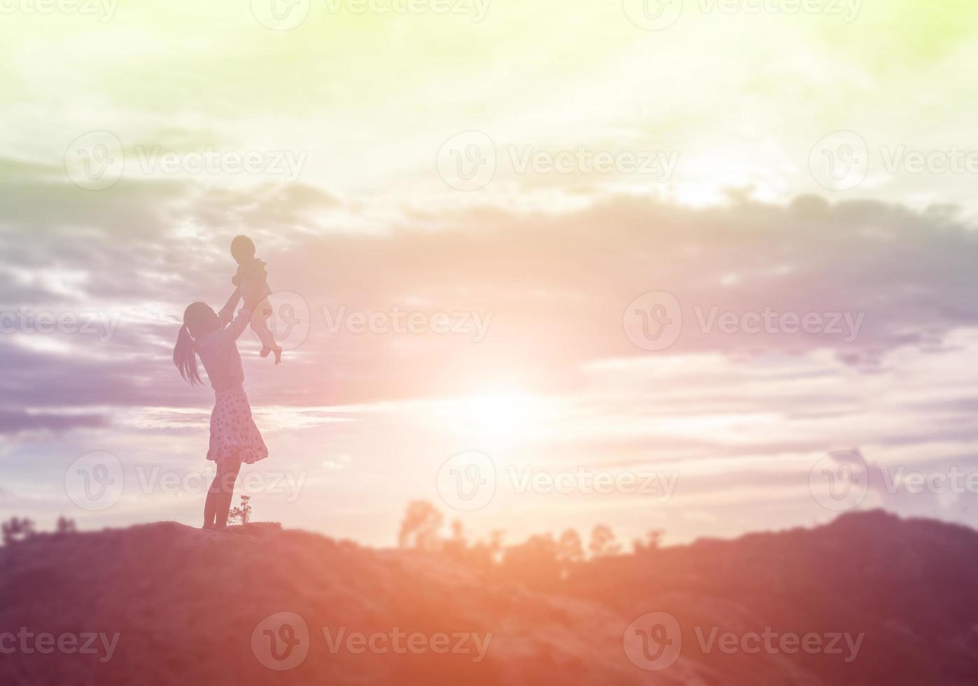 una silueta de una niña feliz los brazos de su madre amorosa para un abrazo, frente a la puesta de sol en el cielo en un día de verano. foto