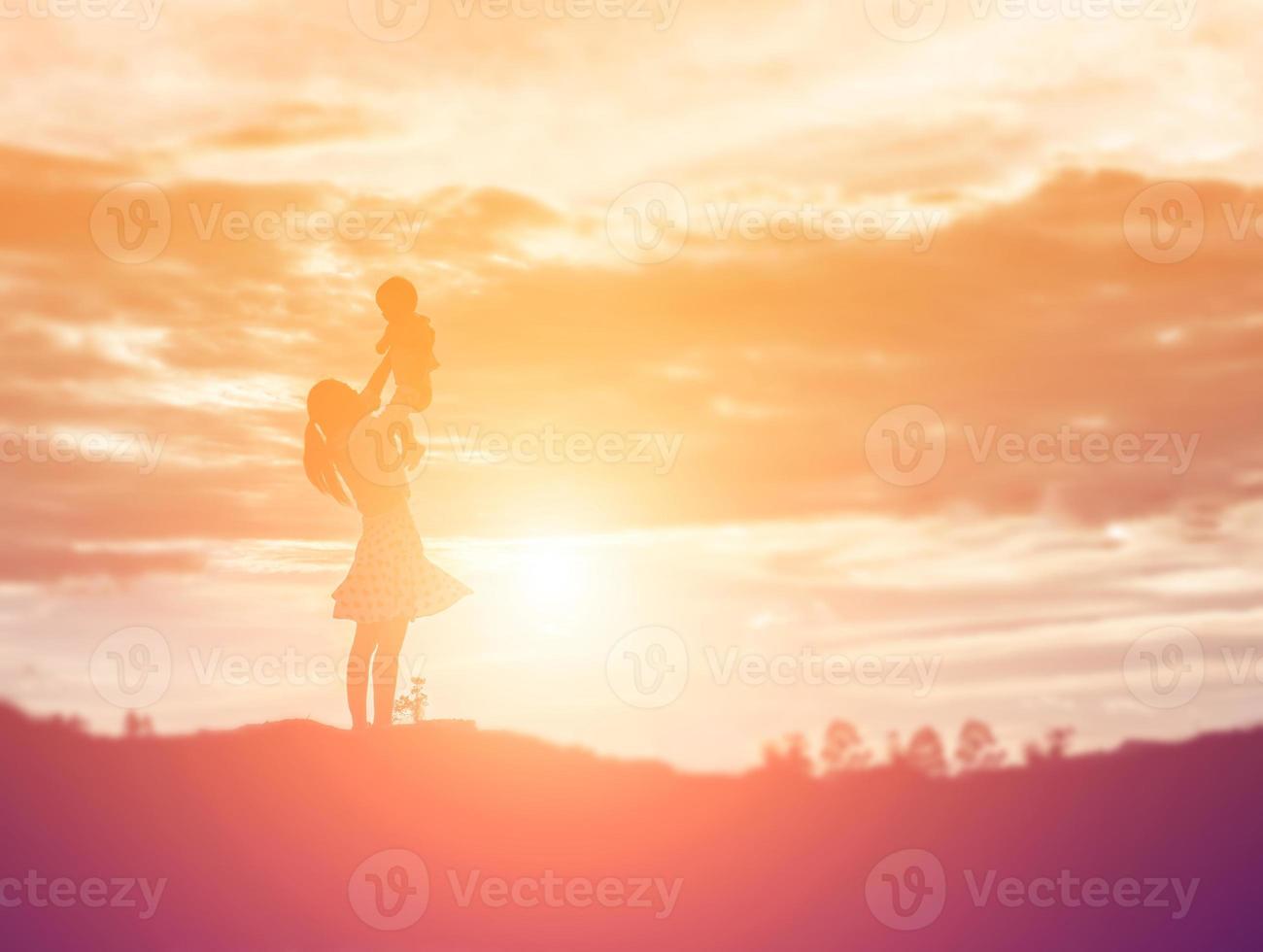 una silueta de una niña feliz los brazos de su madre amorosa para un abrazo, frente a la puesta de sol en el cielo en un día de verano. foto