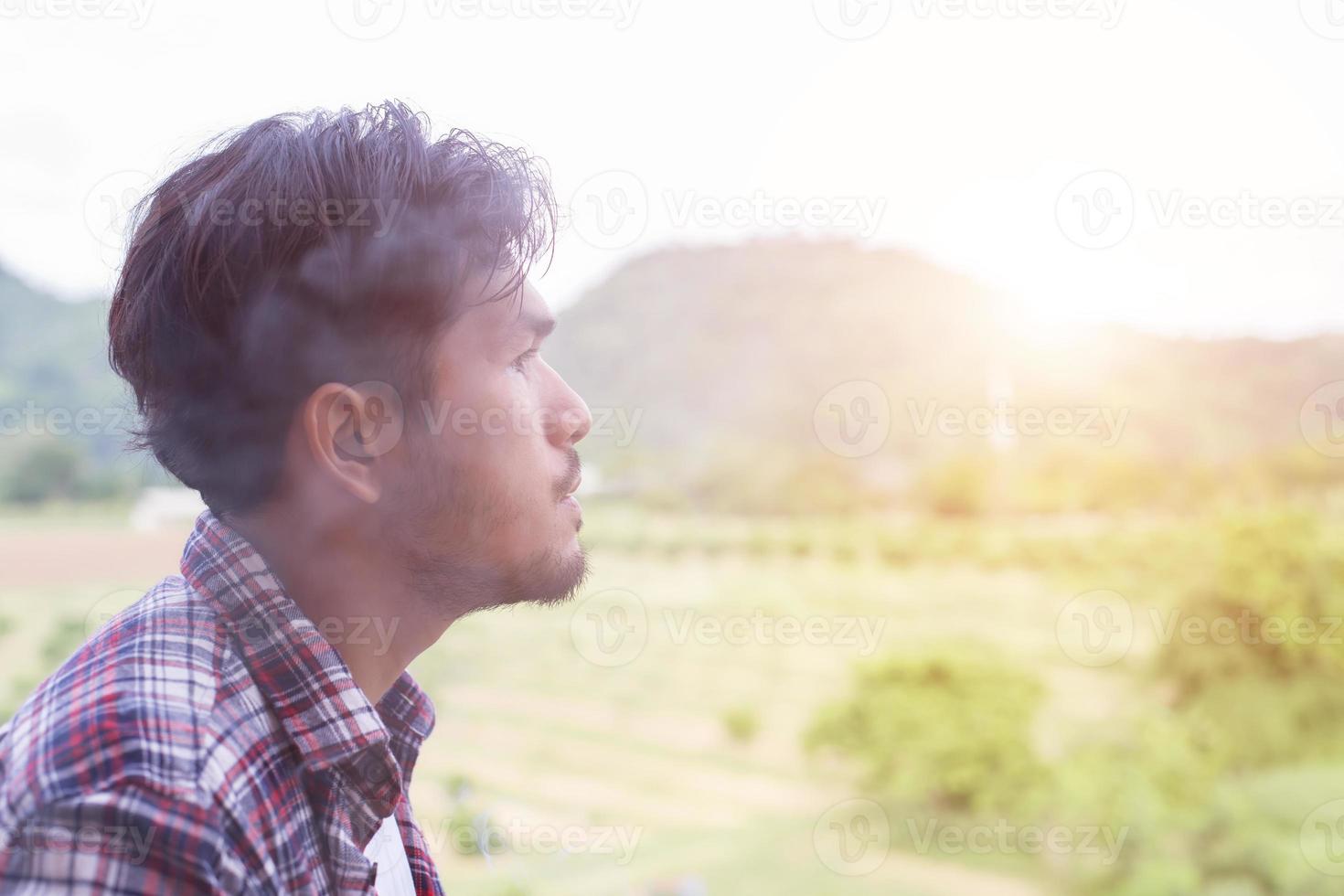 Hipster man smoking cigarette, standing behind a mountain. Among the fresh air in the morning. photo