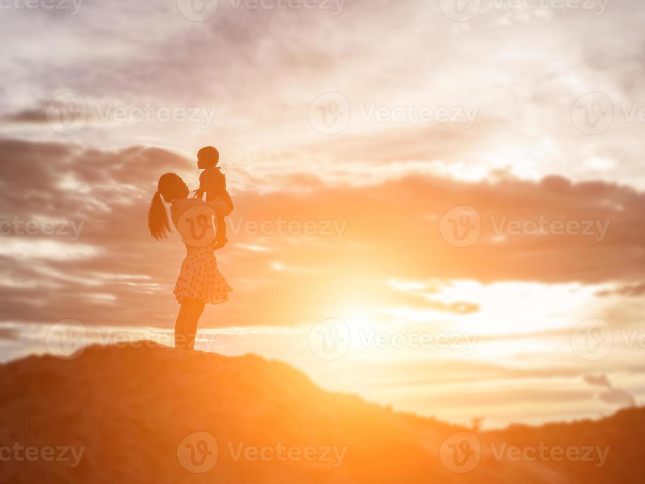 a silhouette of a happy young girl child the arms of his loving mother for a hug, in front of the sunset in the sky on a summer day. photo